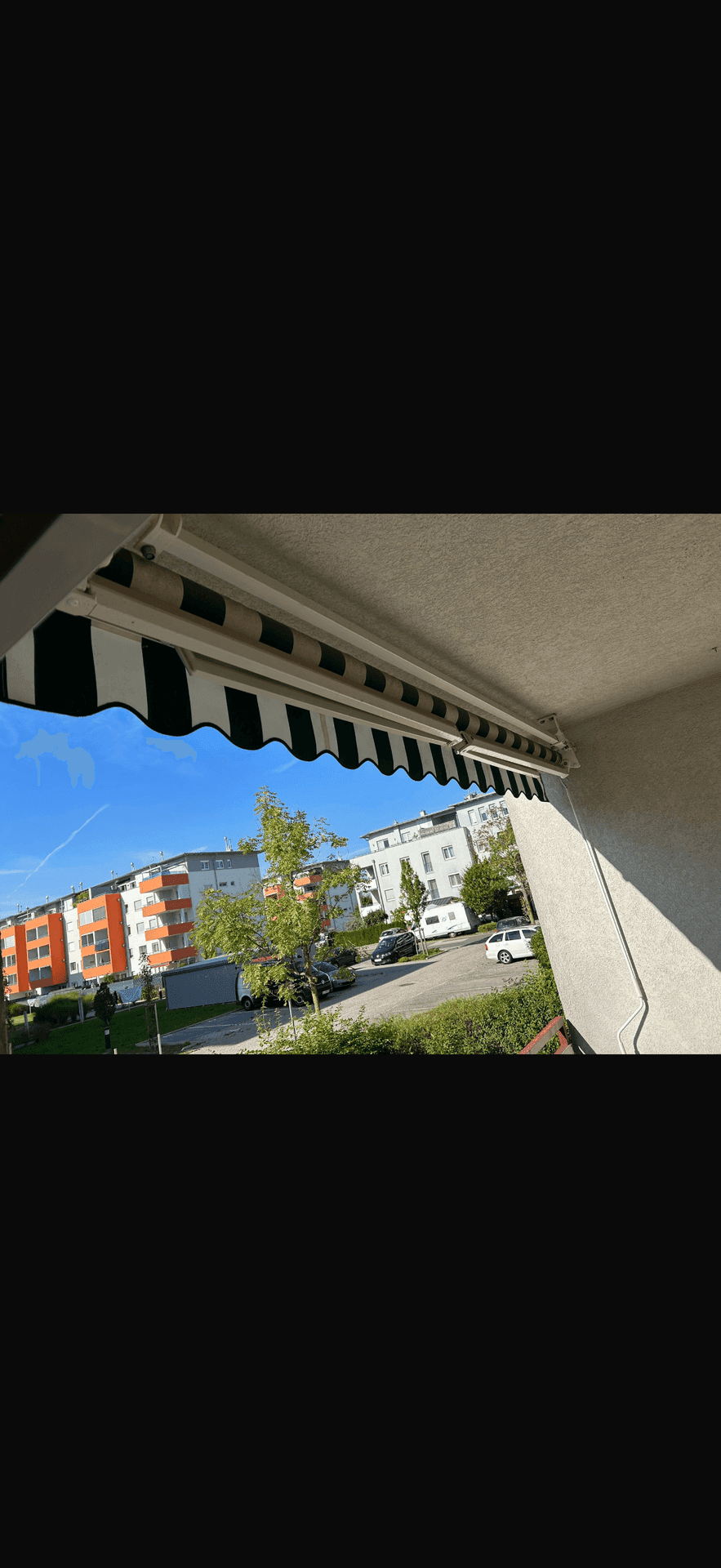 Balkon mit ausgefahrener Markise bietet Schatten und Blick auf die Wohngegend.