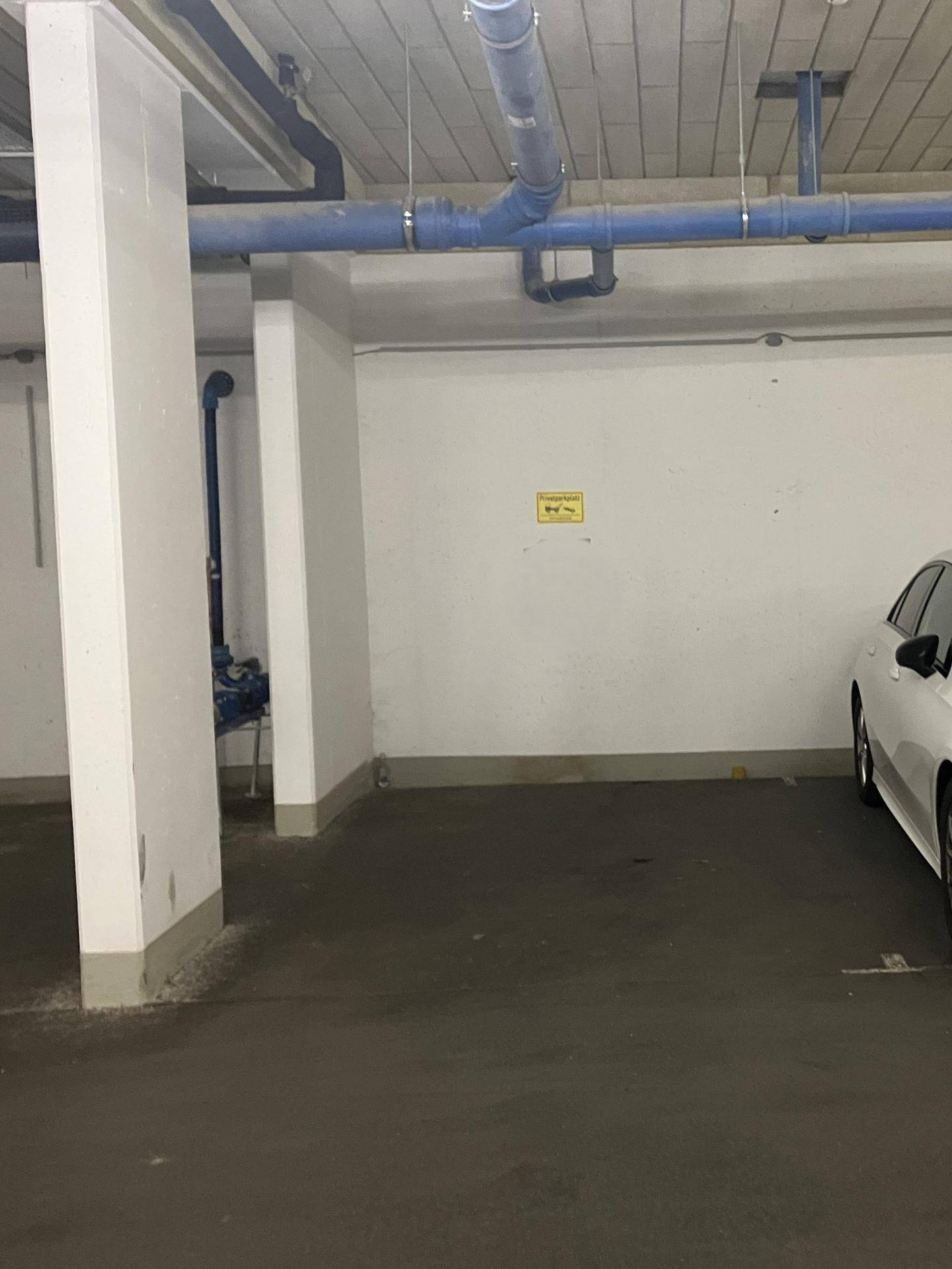 Detailansicht eines Stellplatzes in der Tiefgarage mit blauen Rohren und weiß gestrichenen Wänden.