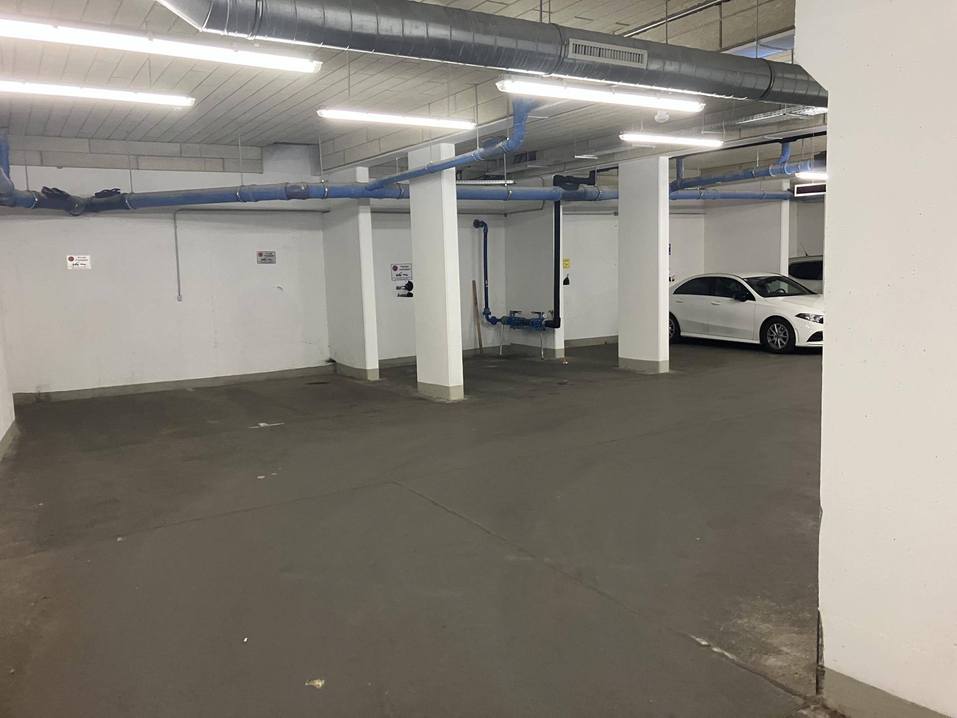Geräumige Tiefgarage mit Betonboden und sichtbaren Versorgungsleitungen an der Decke.