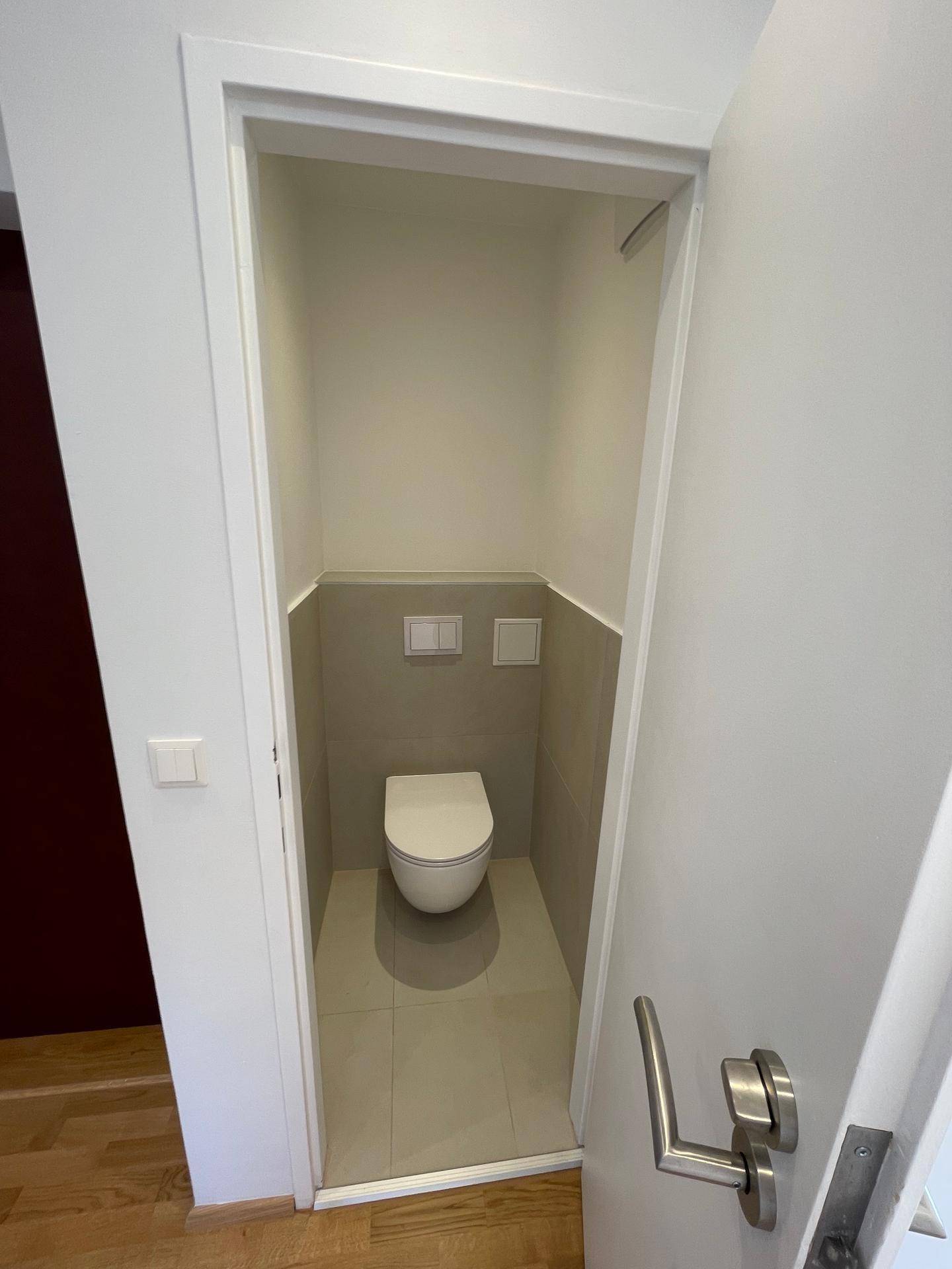 Separates Gäste-WC mit Wand-WC und halbhohen Fliesen in neutralen Farben.