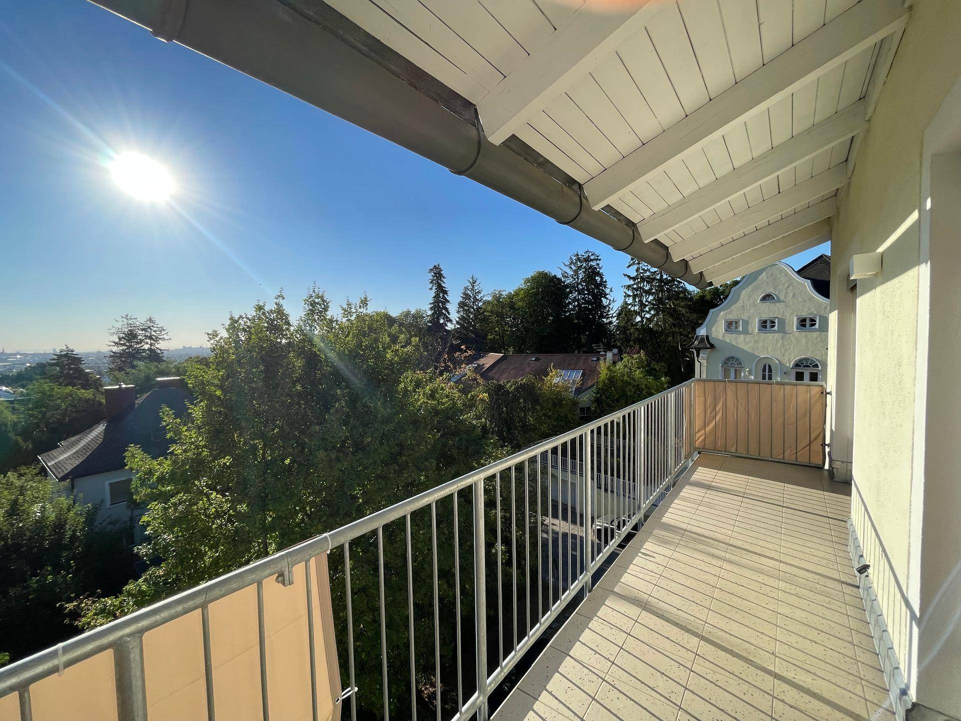 Sonniger Balkon mit Fliesenboden und weitem Blick über die grüne Umgebung.