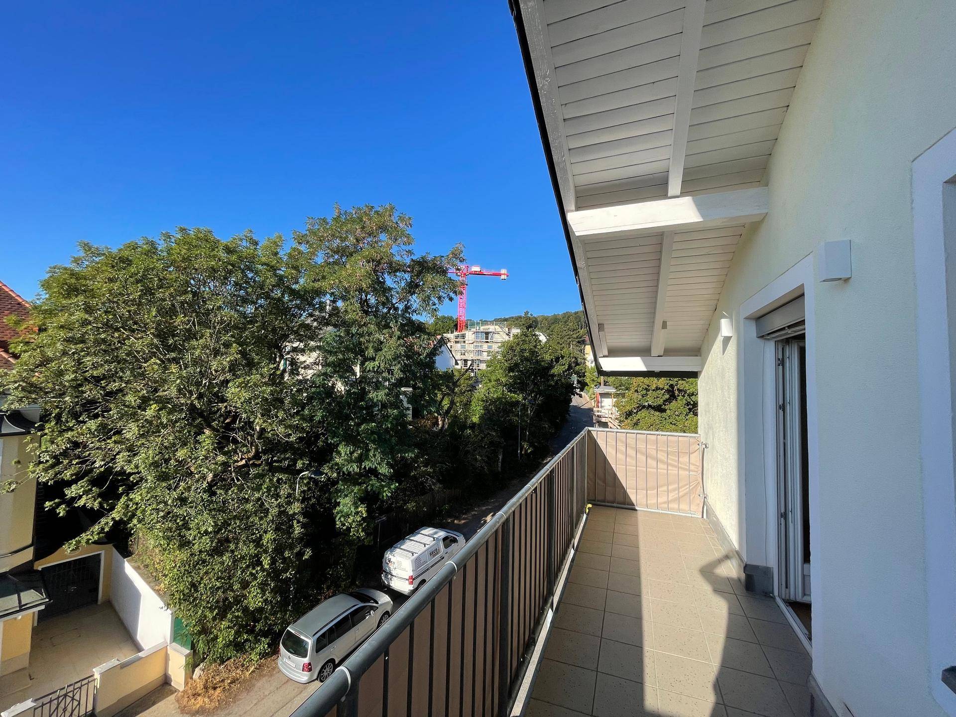 Langer Balkon mit Fliesenboden und Blick auf die grüne Umgebung und eine Baustelle.