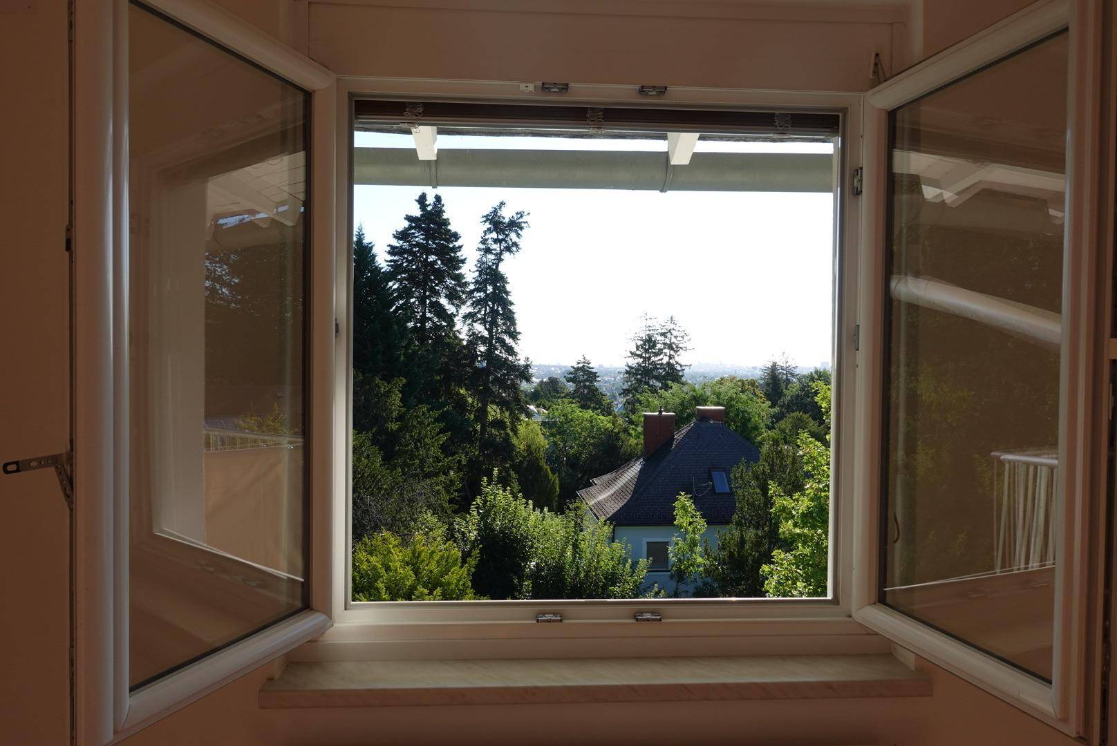 Offenes Fenster bietet einen weiten Blick auf die umliegende grüne Landschaft und Dächer.