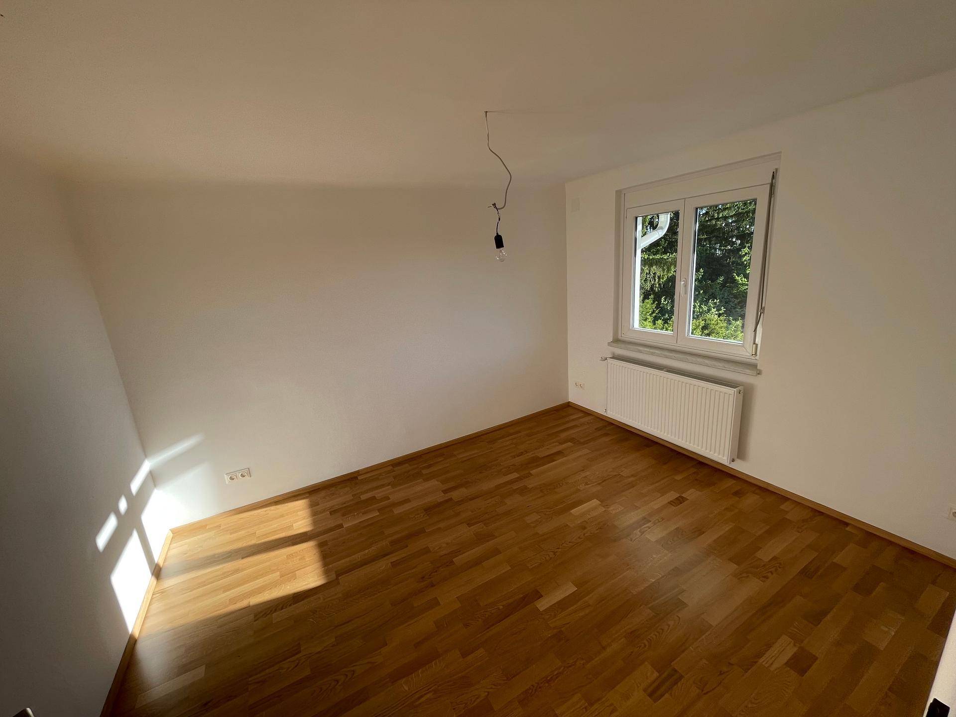 Helles Schlafzimmer mit Holzboden und weiß gestrichenen Wänden, bereit zur Einrichtung.