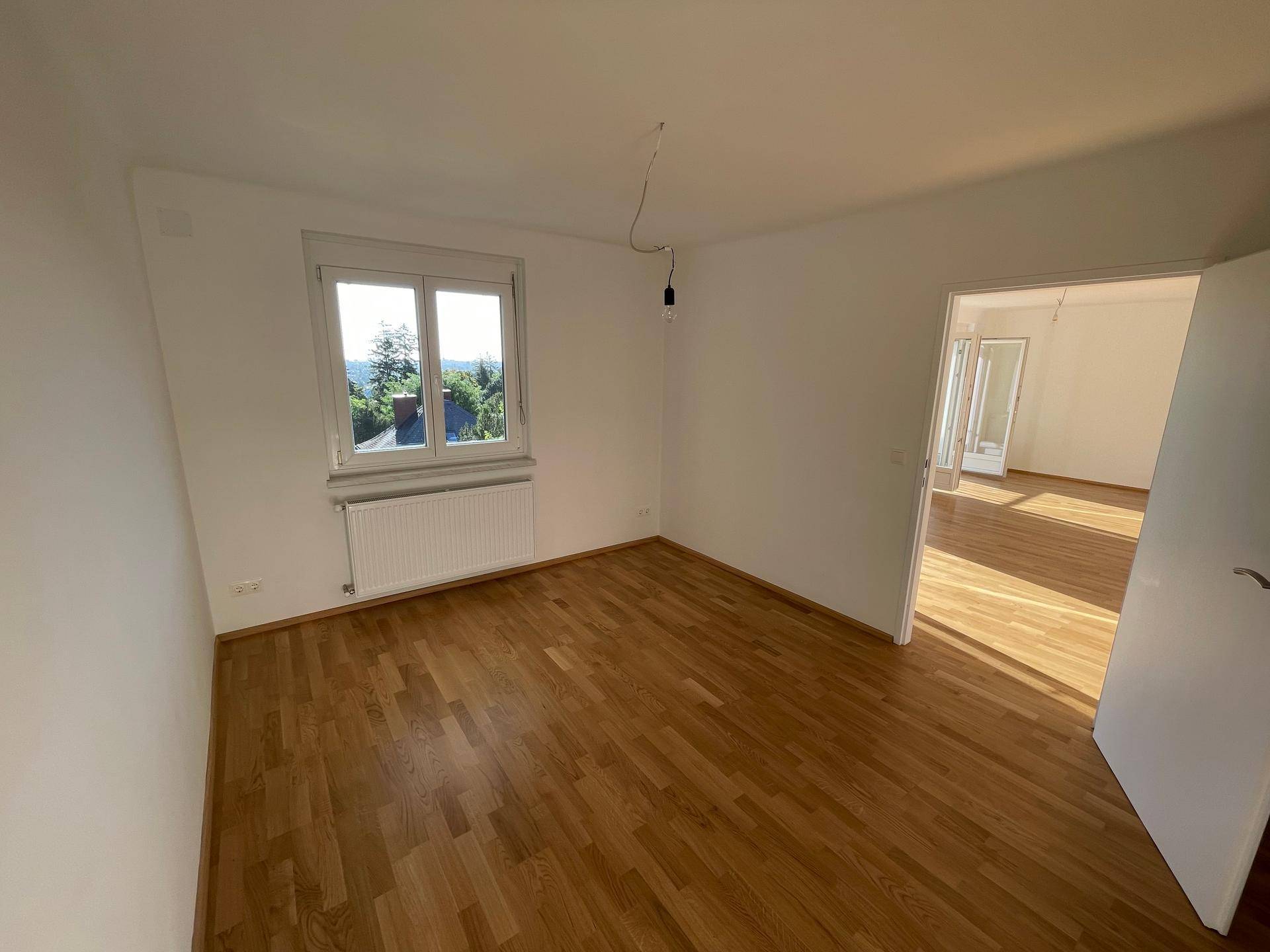 Geräumiges Schlafzimmer mit Parkettboden und einem Fenster mit Blick ins Grüne.