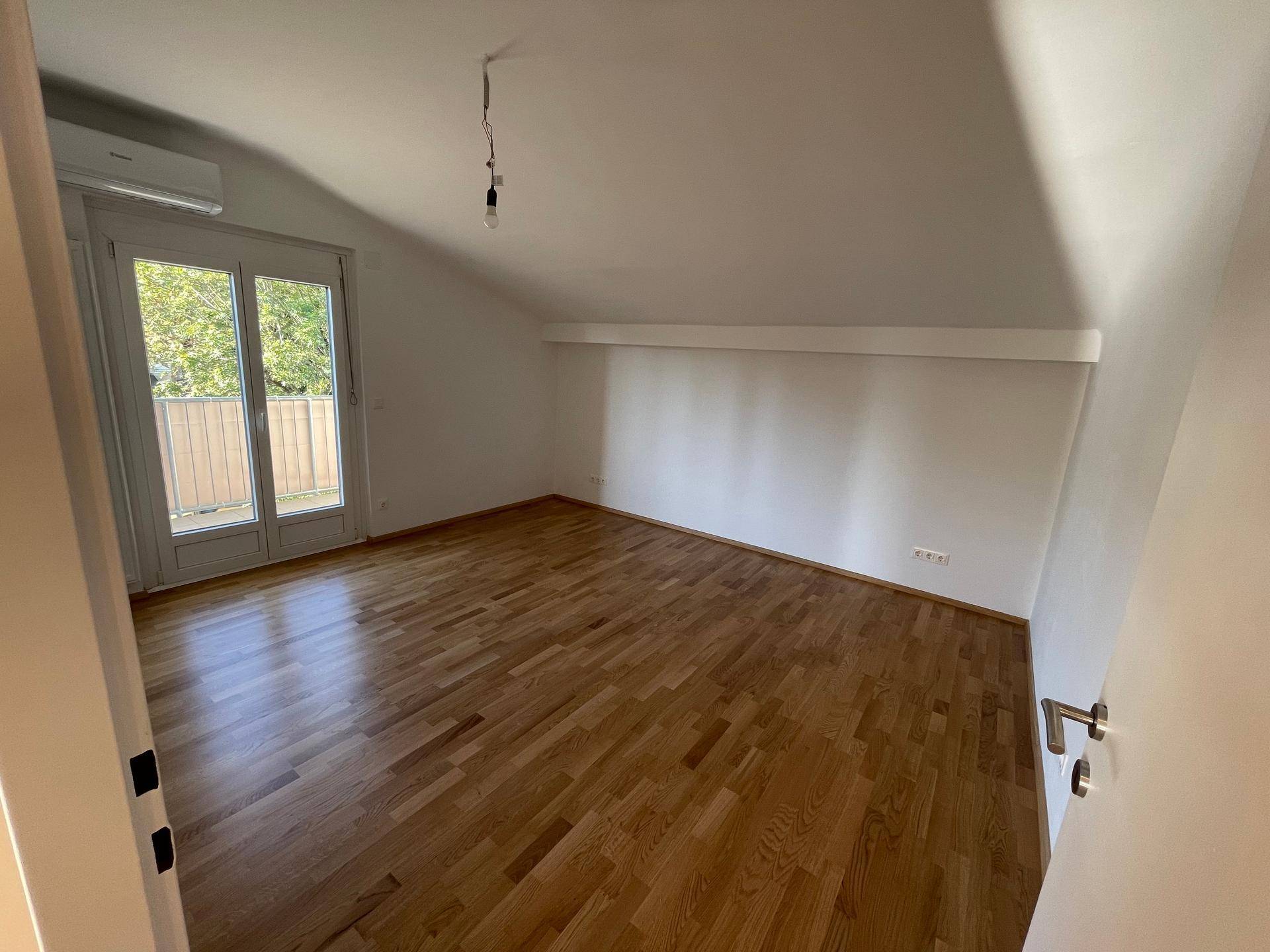 Dachgeschoss-Schlafzimmer mit Holzboden, Klimaanlage und Zugang zu einem französischen Balkon.