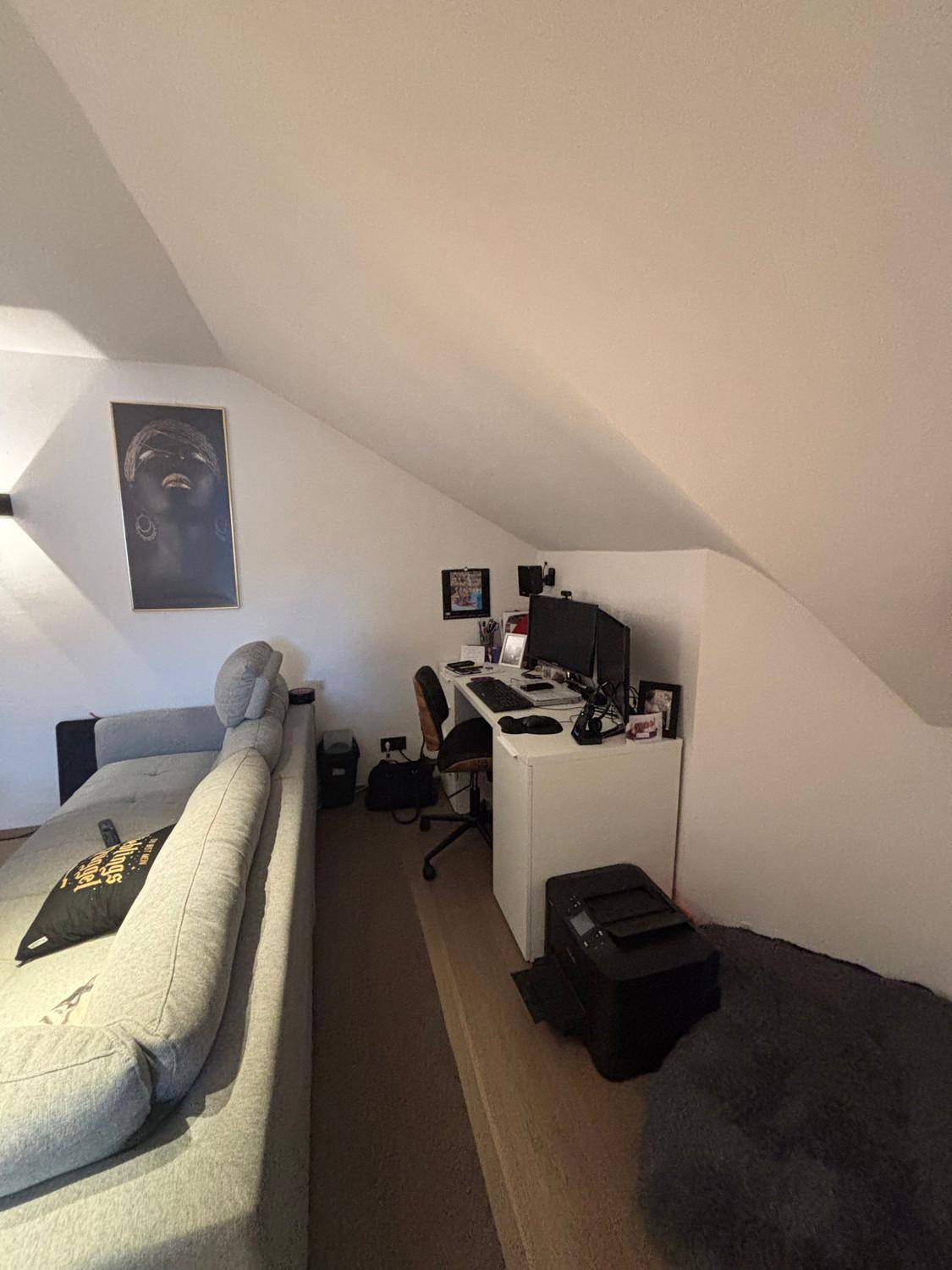 Schlafzimmer mit Schreibtischbereich unter der Dachschräge und modernem Sofa.
