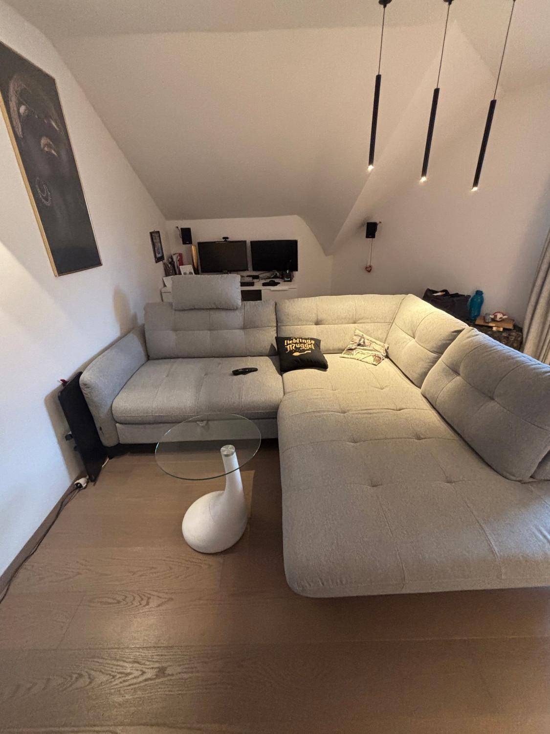 Gemütliches Wohnzimmer mit großem Ecksofa, Glastisch und Dachschräge.
