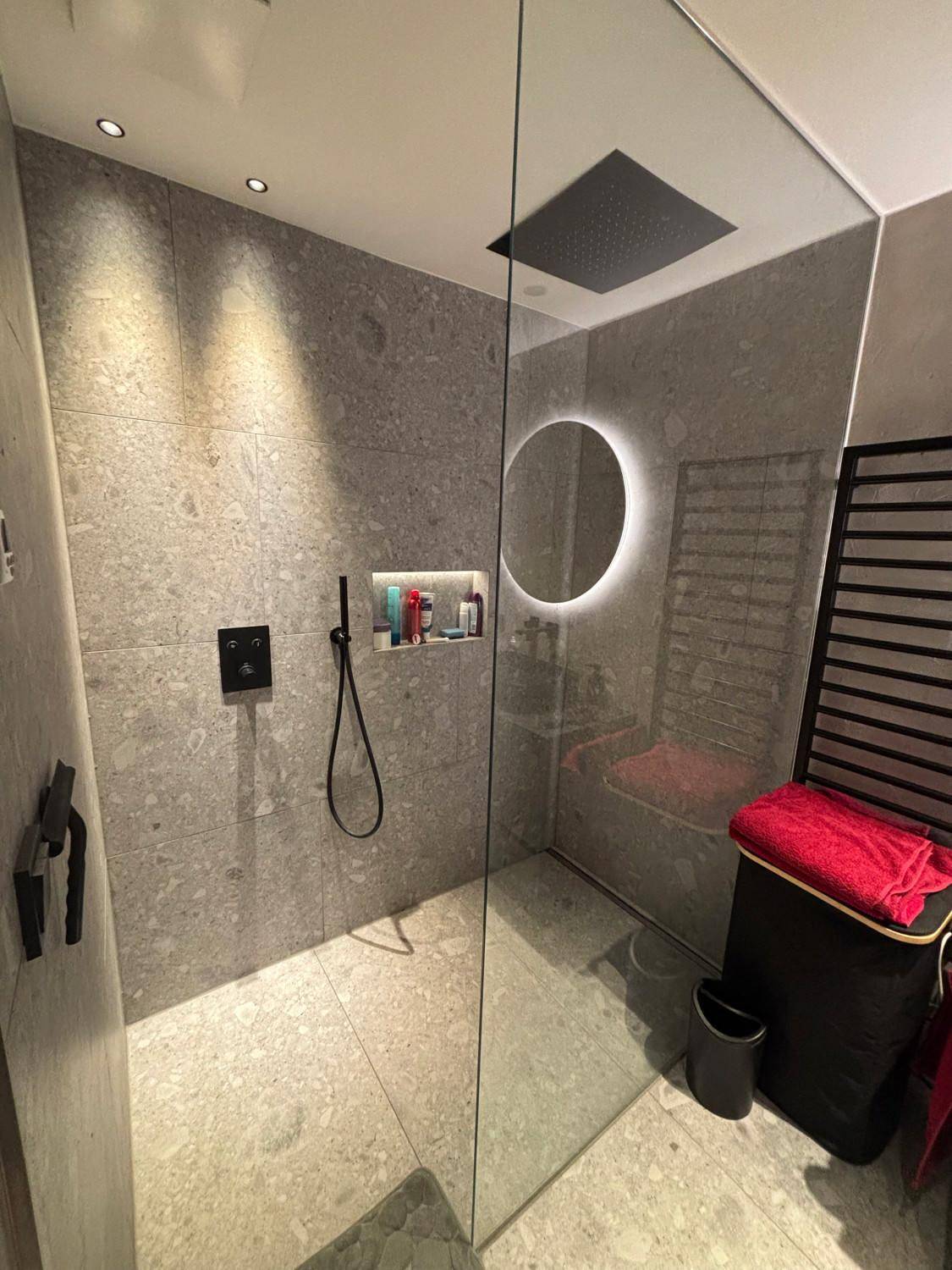 Elegantes Badezimmer mit großer begehbarer Dusche, grauen Fliesen und modernem Design.