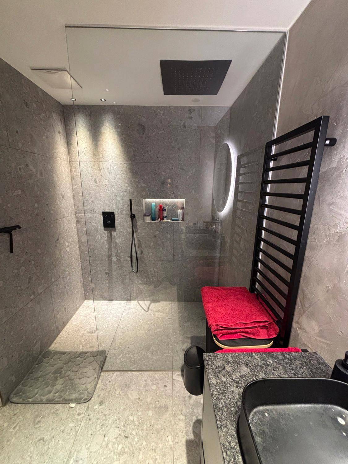 Modernes Badezimmer mit begehbarer Dusche, grauen Fliesen und schwarzem Handtuchheizkörper.