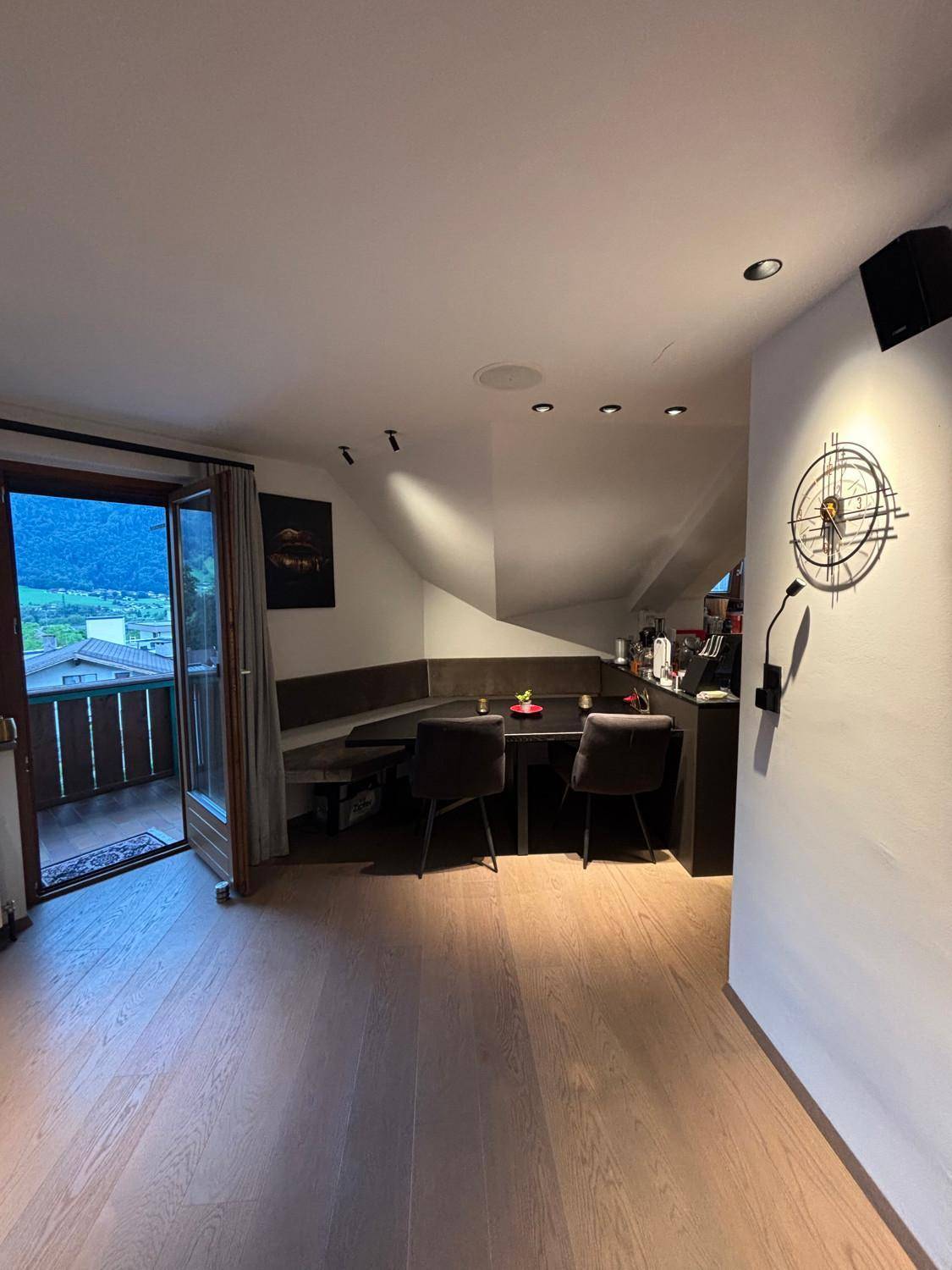 Heller Wohn-Essbereich mit offener Küche, Holzboden und Balkon mit Bergblick.