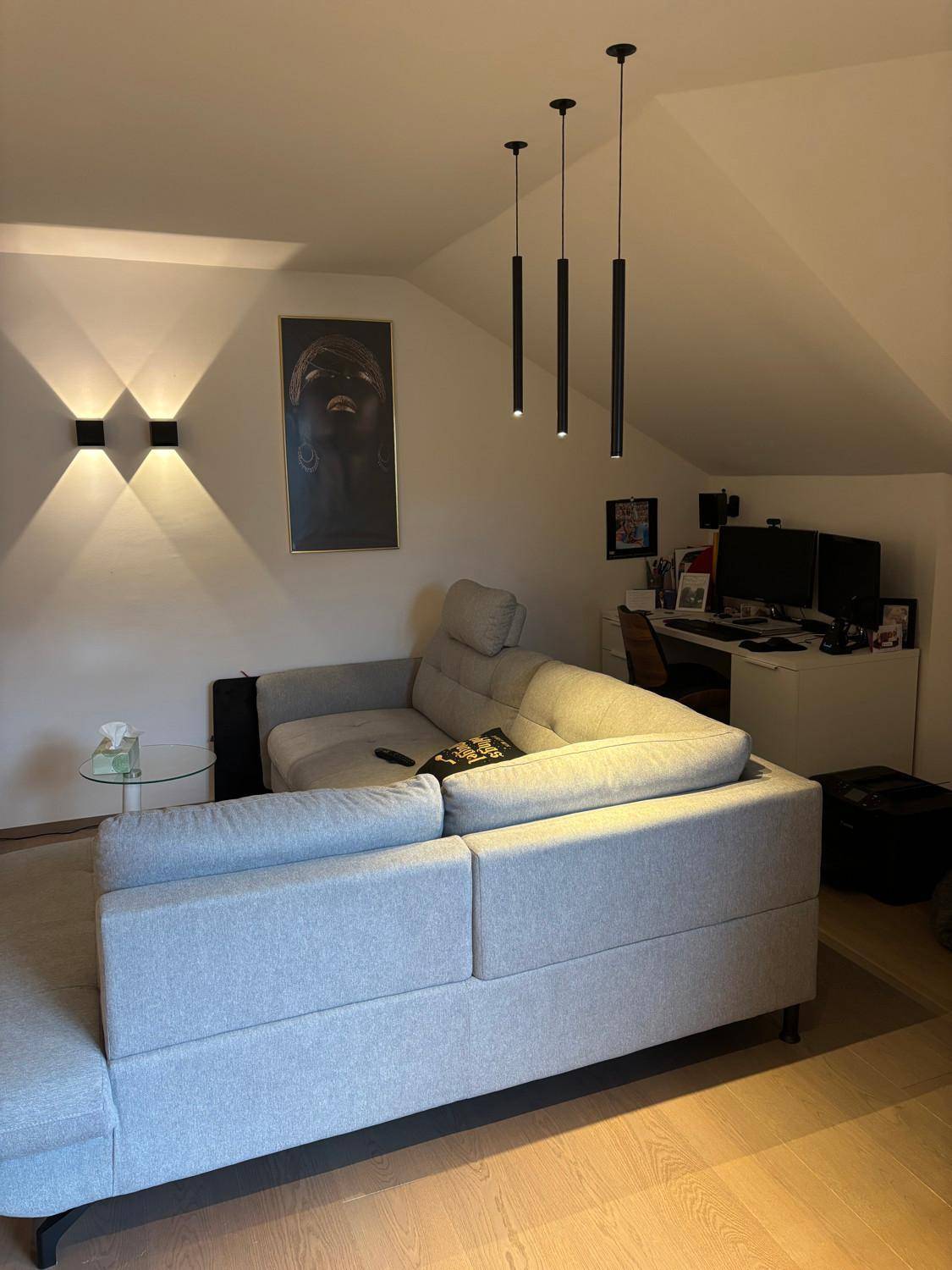 Helles Wohnzimmer mit bequemer Couch, Holzboden und Dachschrägen, inklusive Arbeitsbereich.