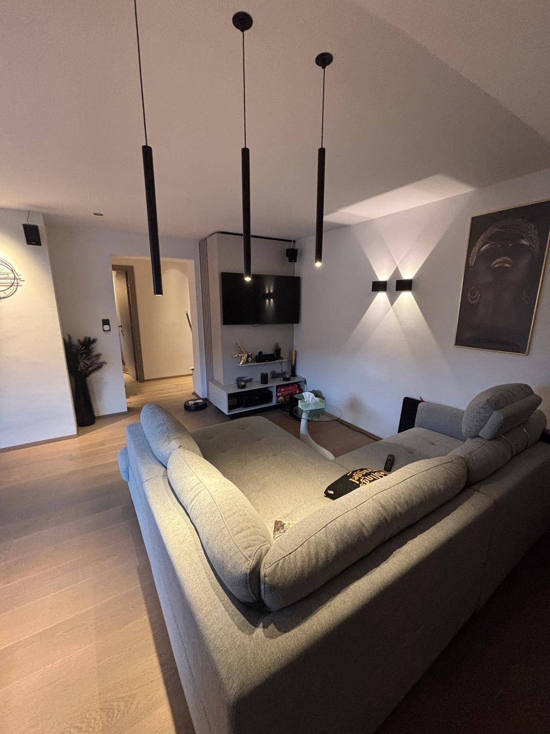 Modernes Wohnzimmer mit großem Sofa, Fernseher und stilvoller Beleuchtung.