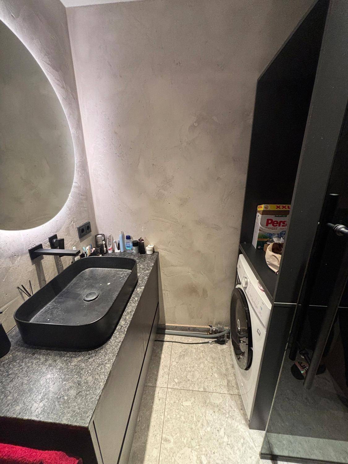 Modernes Badezimmer mit schwarzem Waschbecken, beleuchtetem Spiegel und integrierter Waschmaschine.