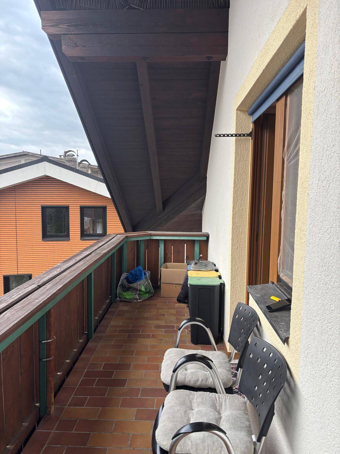 Schmaler Balkon mit Holzgeländer und Fliesenboden, bietet Platz für Sitzgelegenheiten.