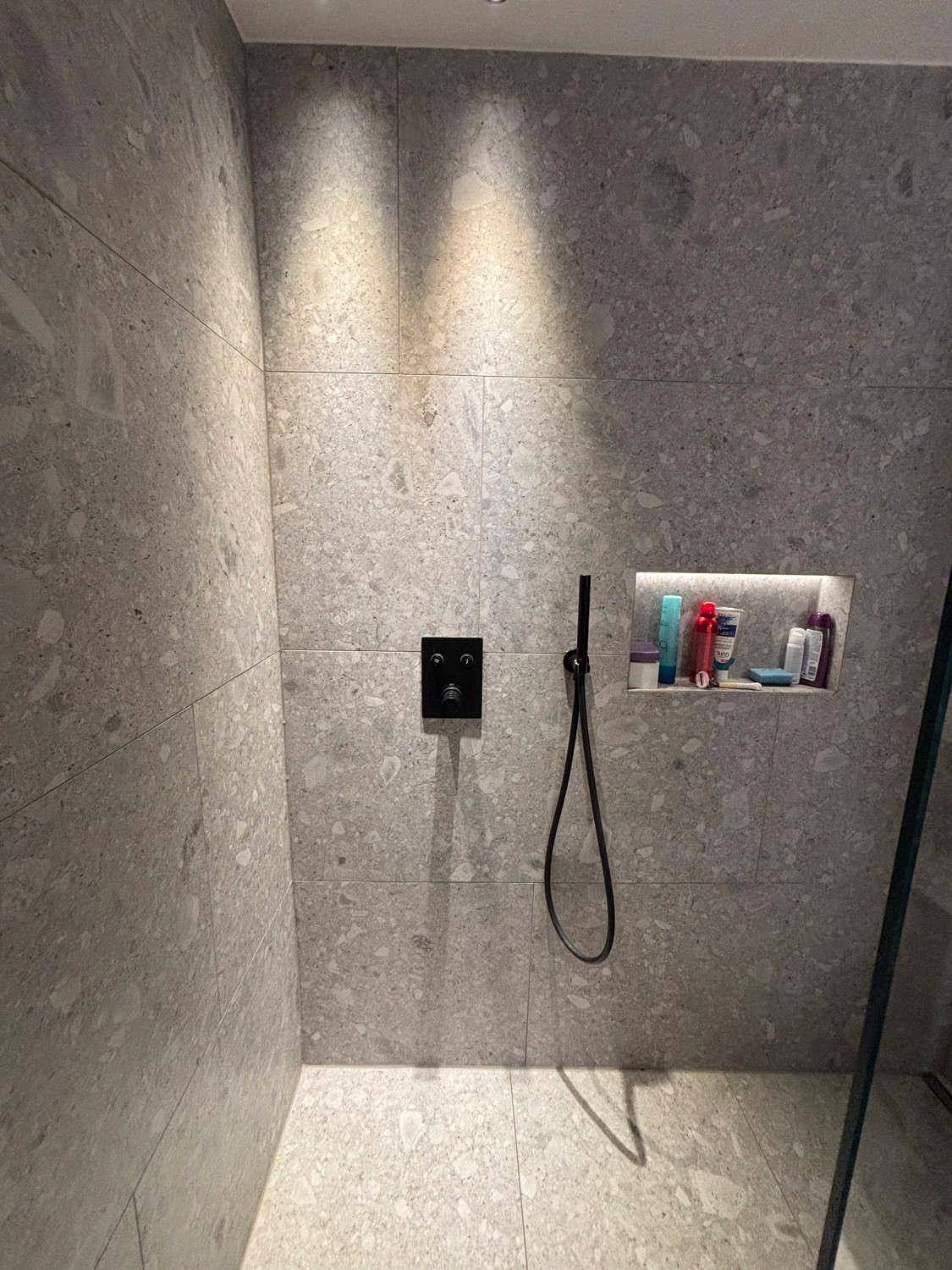 Detailansicht der modernen, begehbaren Dusche mit grauen Fliesen und schwarzen Armaturen.