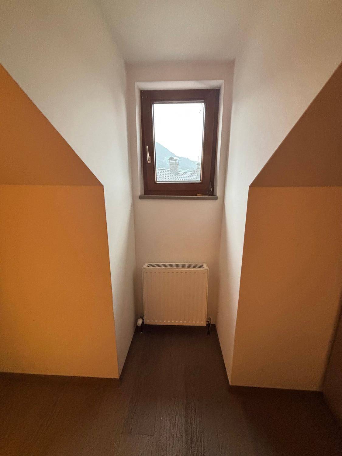 Kleines Fenster in einer Dachschräge mit Heizkörper darunter und dunklem Boden.