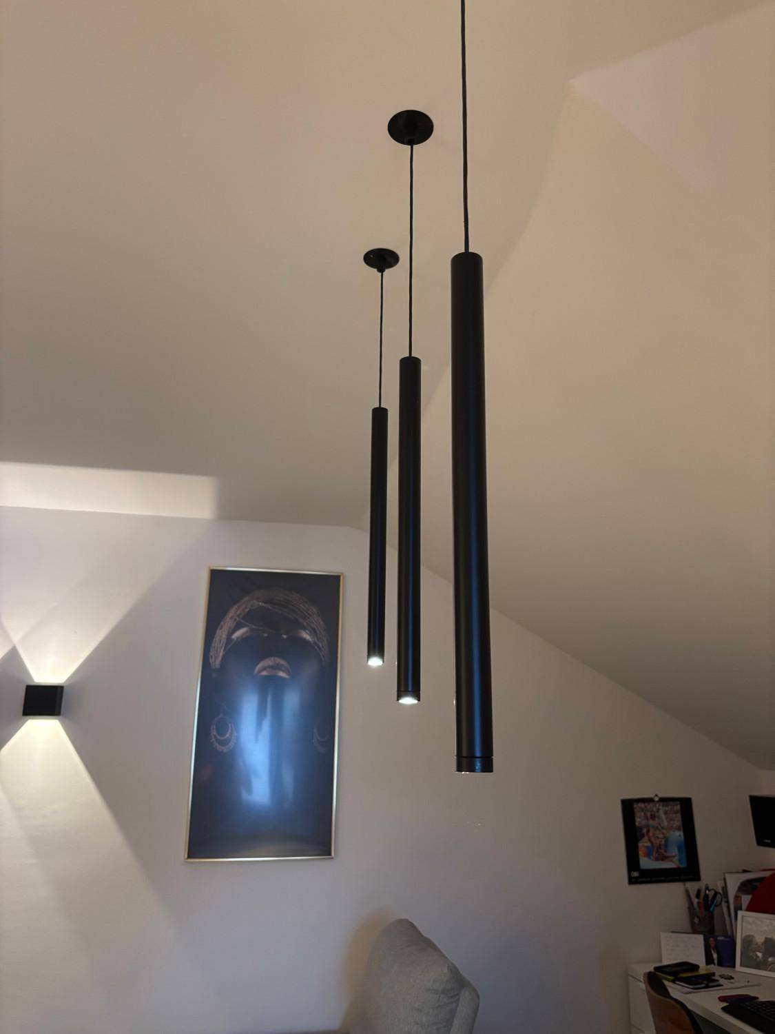 Moderne schwarze Pendelleuchten an der schrägen Decke über einem Kunstwerk.