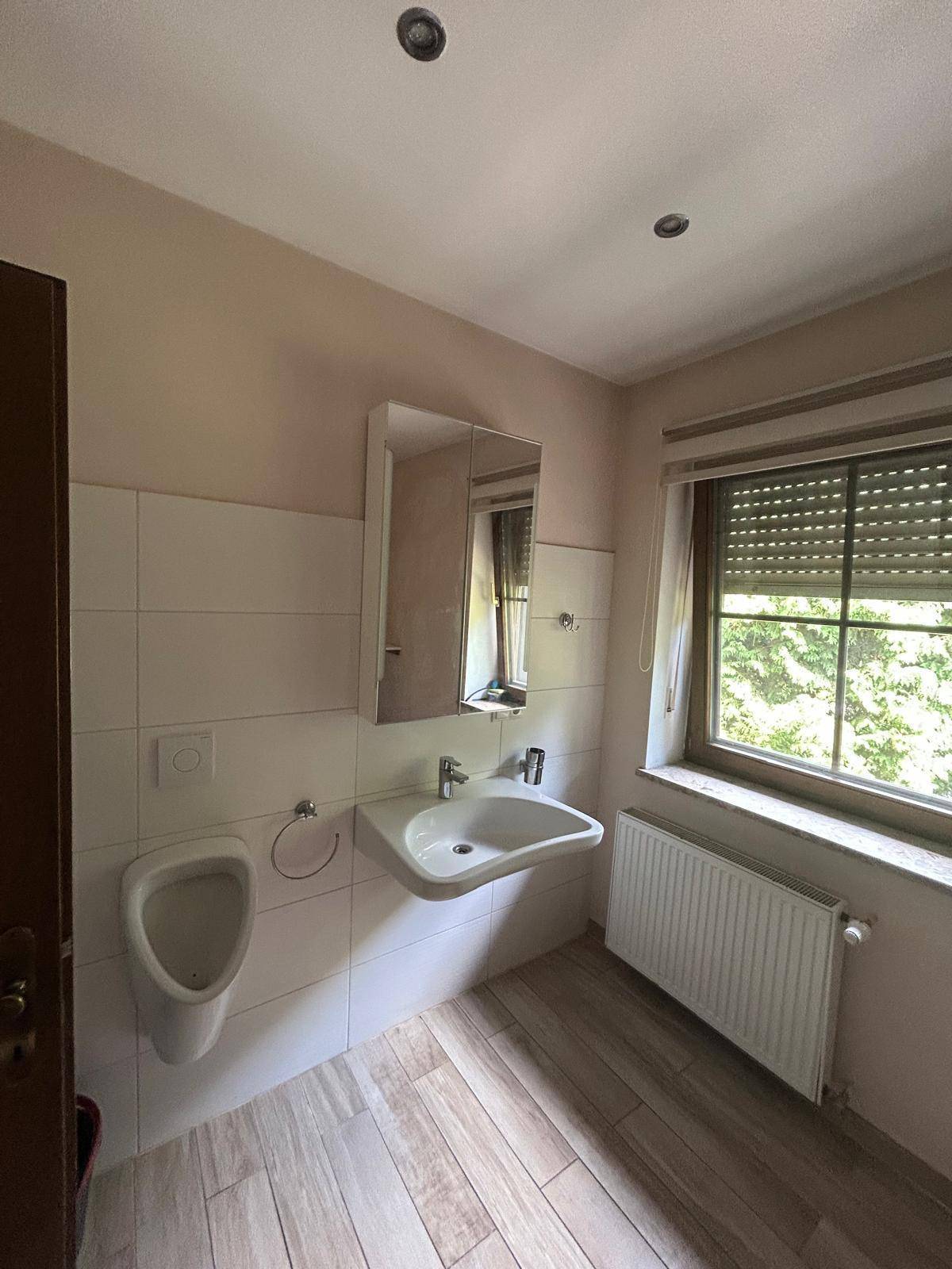 Modernes Gäste-WC mit Urinal, Waschbecken und Fenster, hell gefliest.