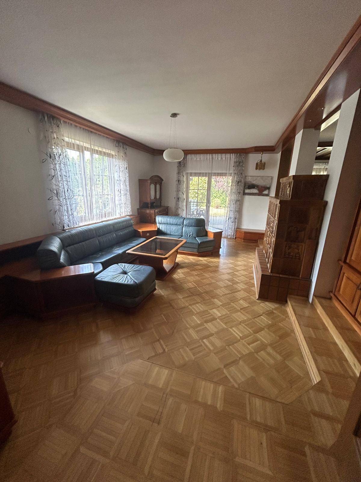 Gemütliches Wohnzimmer mit Parkettboden, Kachelofen und Ledersofas, mit Zugang zum Garten.