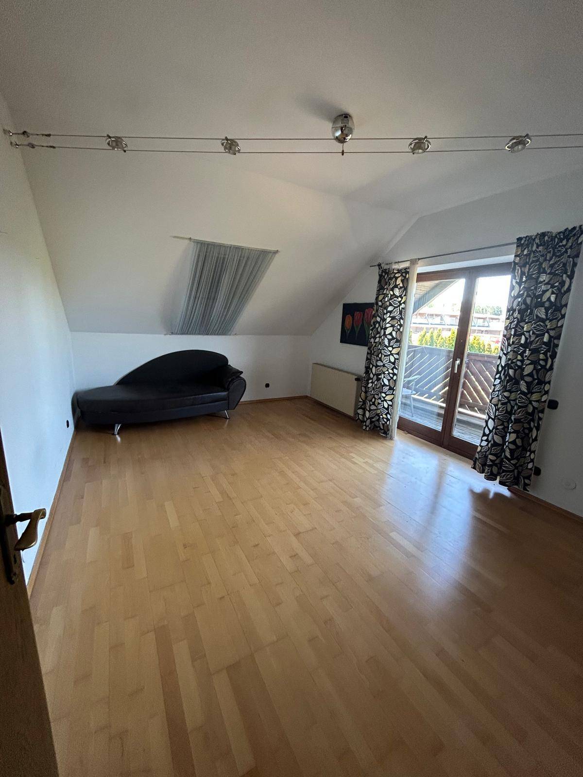 Geräumiges Schlafzimmer mit Holzboden, Dachschräge und Zugang zu einem Balkon.