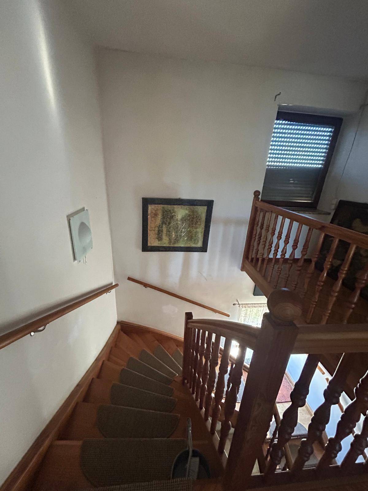 Holztreppe mit Teppichläufer und Geländer, die in die obere Etage führt.