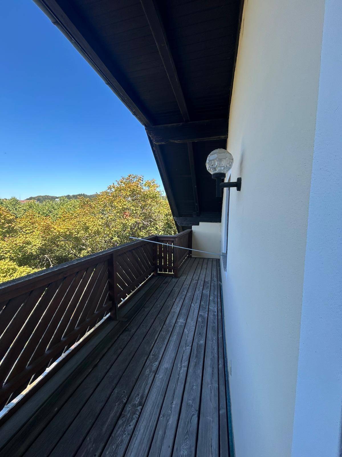 Langer Holzbalkon mit Geländer und Blick auf die umliegende grüne Landschaft.