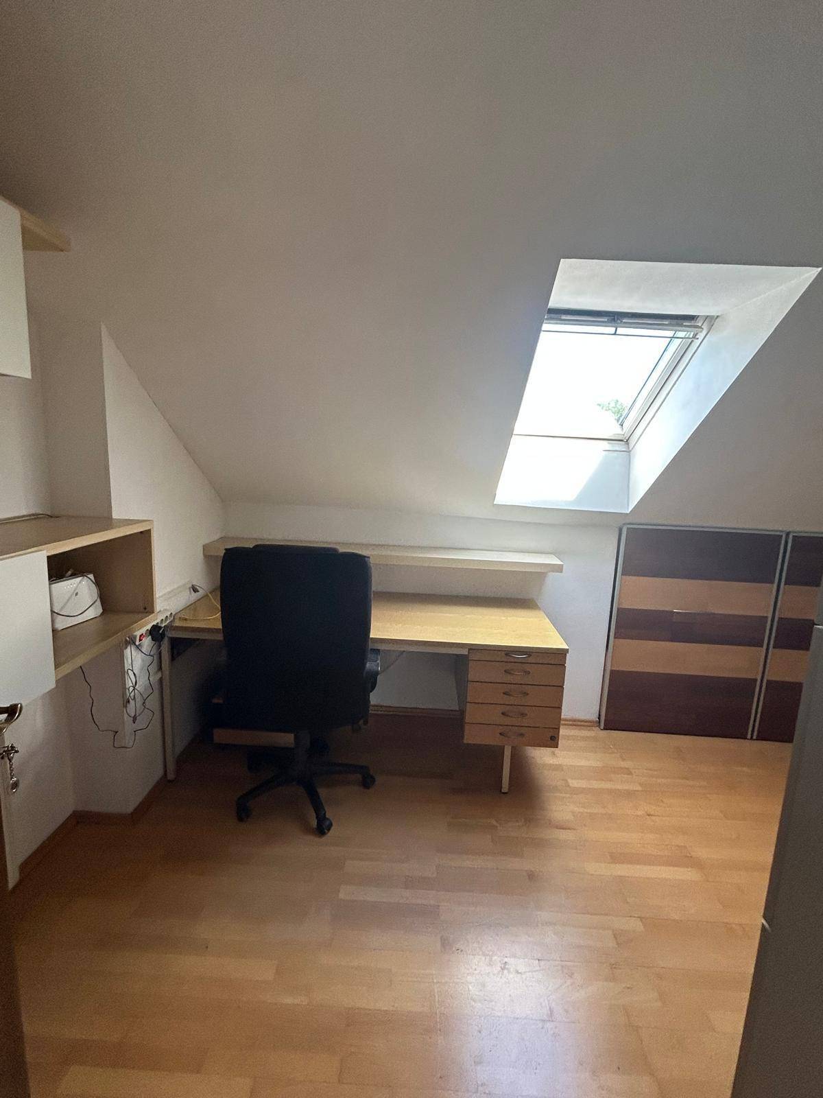 Helles Dachzimmer, eingerichtet als Büro mit Schreibtisch und Dachfenster.