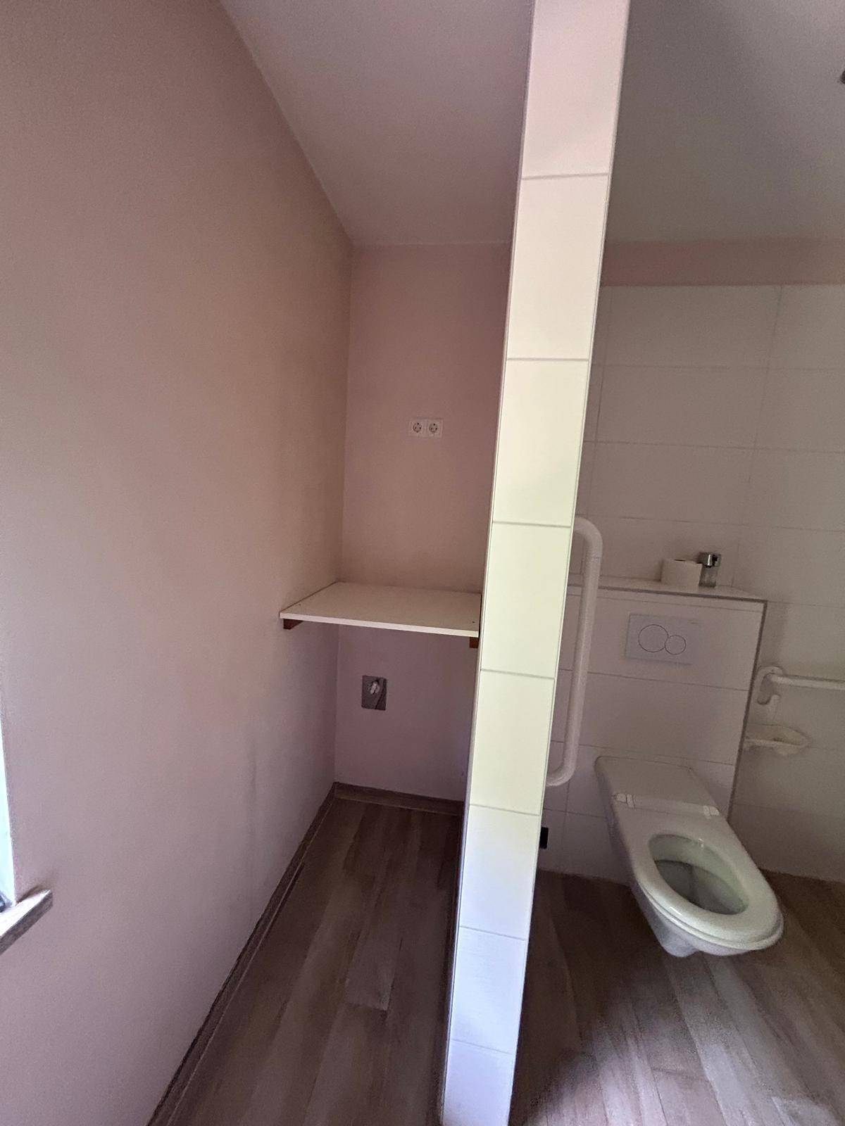 Barrierefreies WC mit Haltegriffen und wandhängender Toilette, in hellen Farben gehalten.