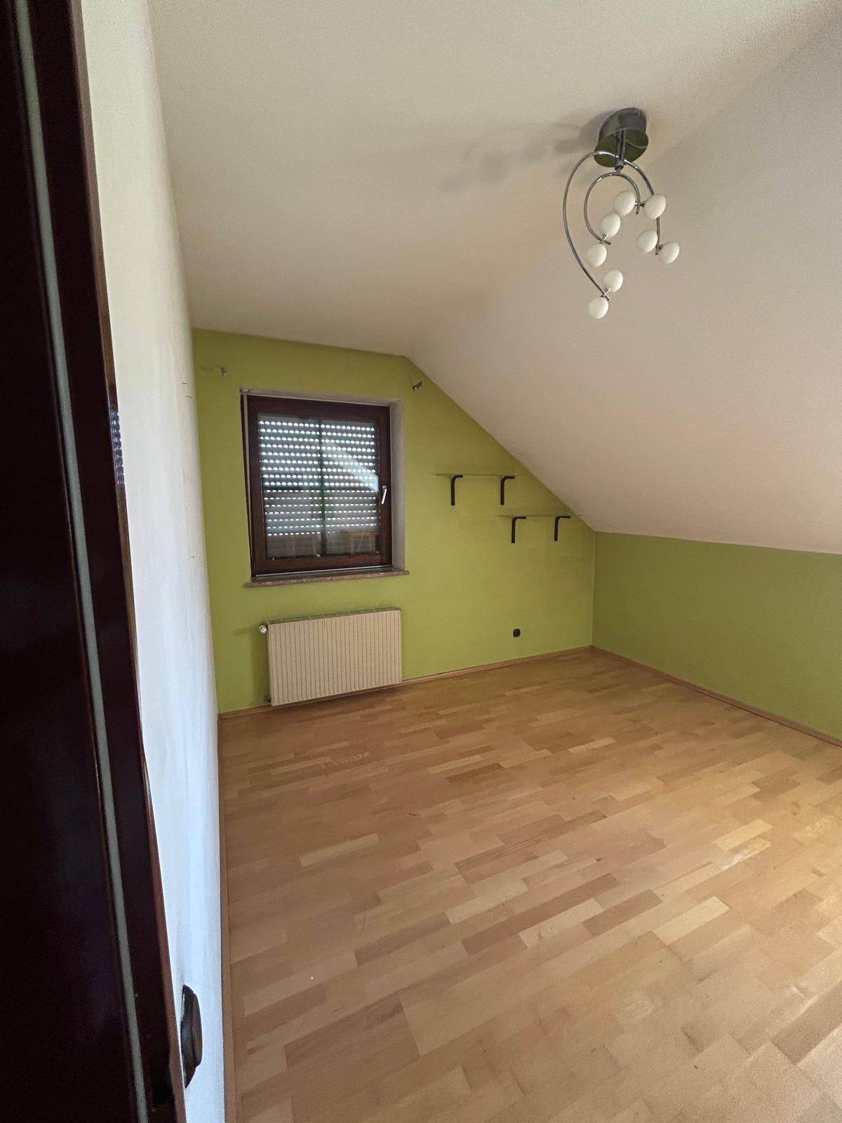 Helles Schlafzimmer mit Dachschräge, grün gestrichenen Wänden und Laminatboden.