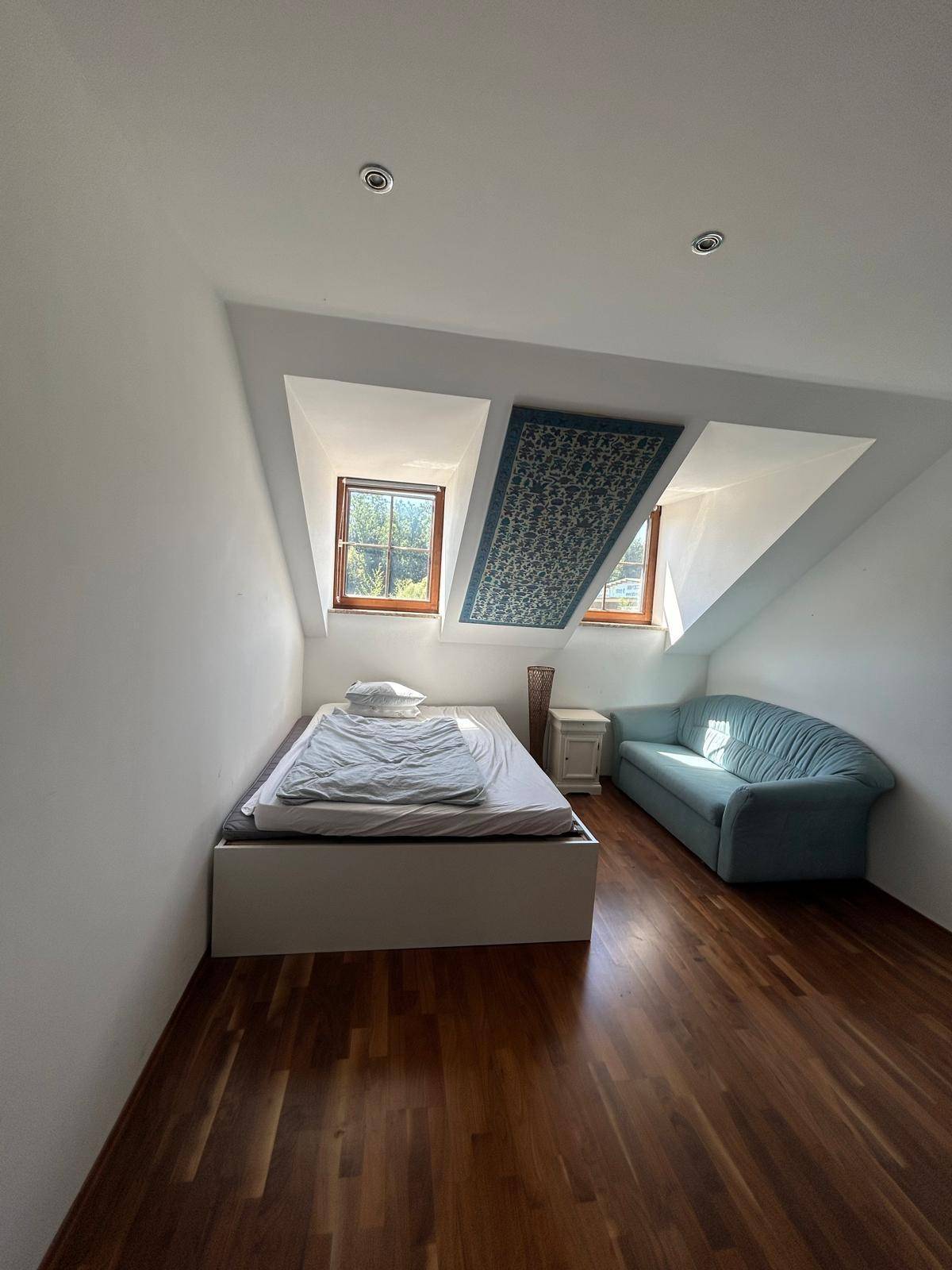 Schlafzimmer mit Holzboden, zwei Dachfenstern und einem Bett, gemütlich eingerichtet.