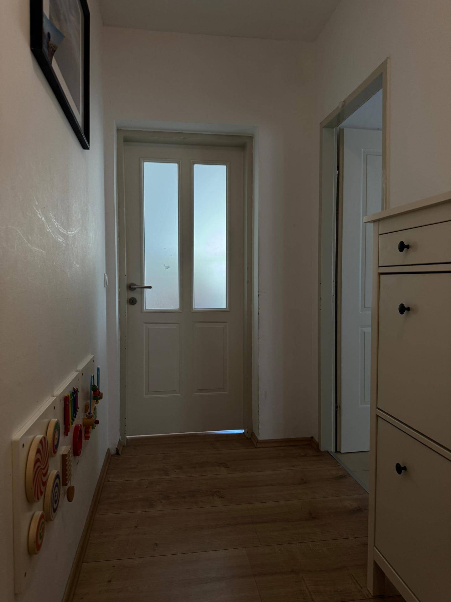 Heller Flur mit Laminatboden und weißer Tür, freundlicher Eingangsbereich mit Spielzeug an der Wand.