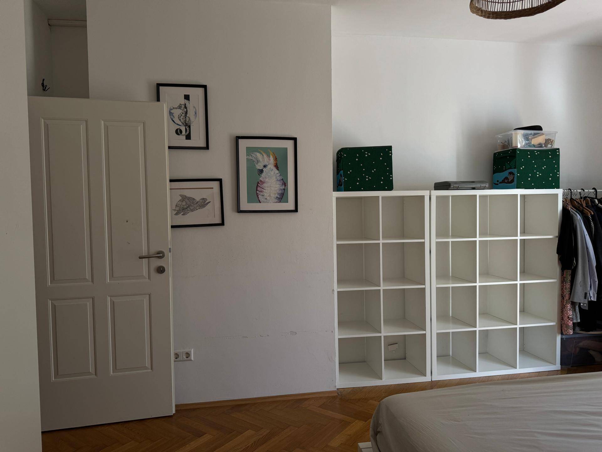 Schlafzimmer mit Parkettboden, weißem Regal und dekorativen Bildern, bietet Stauraum und Komfort.