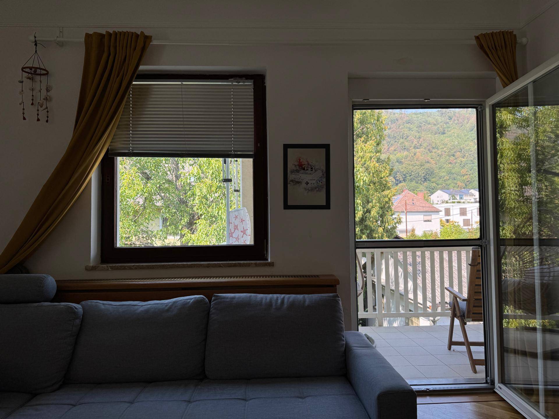 Gemütliches Wohnzimmer mit Sofa und Zugang zum Balkon, bietet einen schönen Blick ins Grüne.