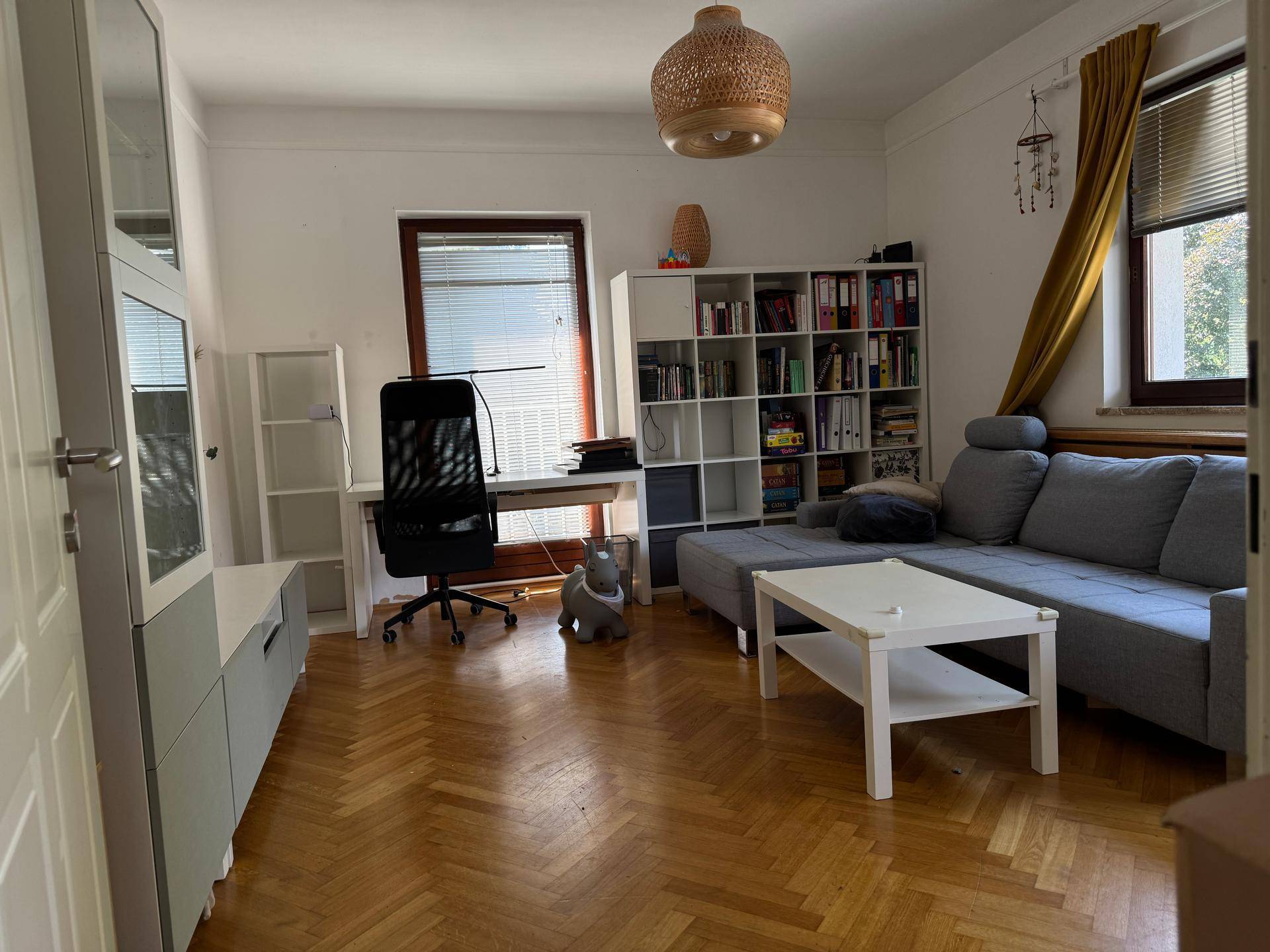 Helles Wohnzimmer mit Fischgrätparkett, Sofa, Schreibtisch und Bücherregalen, vielseitig nutzbar.