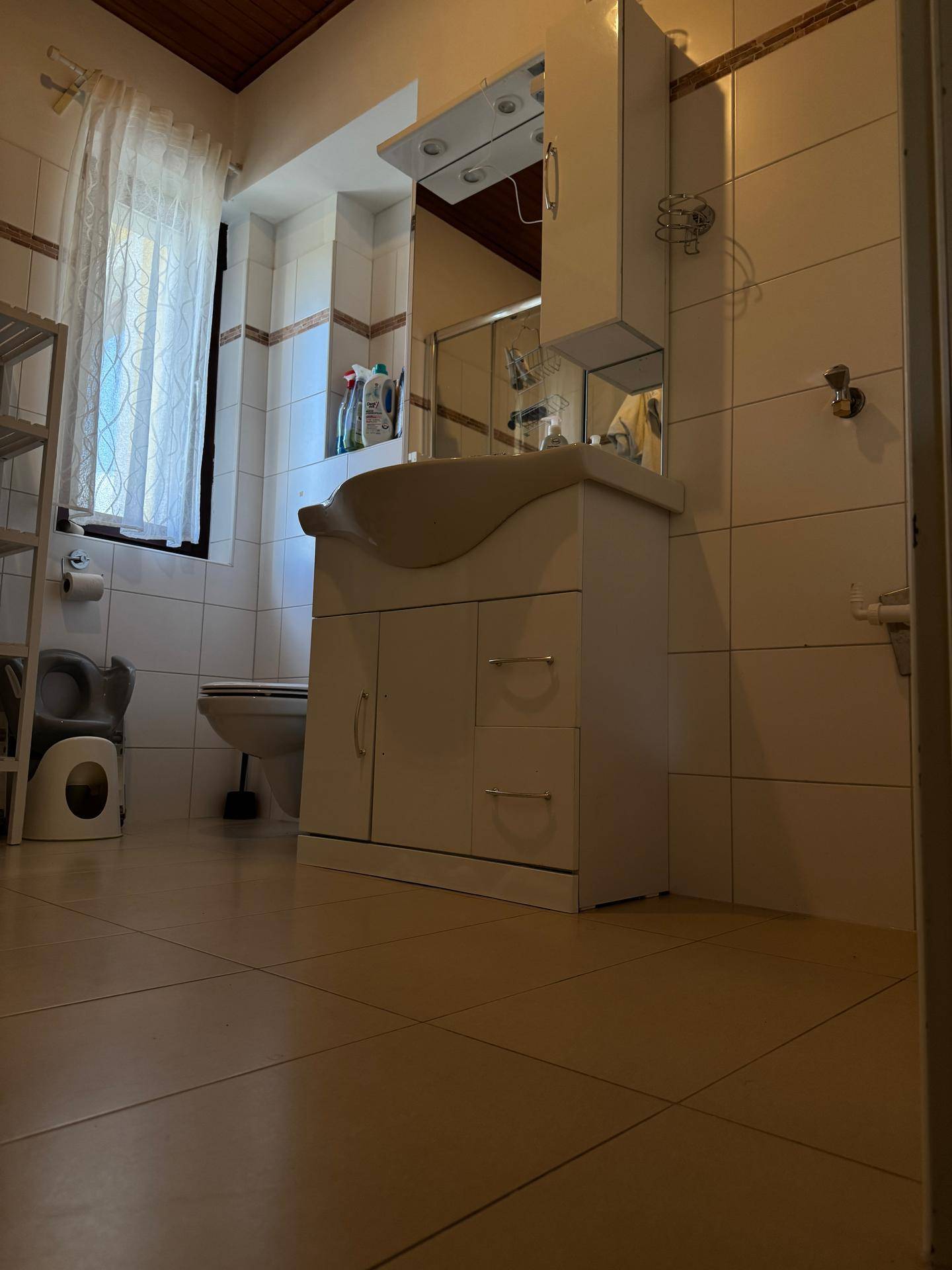 Helles Badezimmer mit WC, Waschtisch und Spiegelschrank, ausgestattet mit Fenster für Tageslicht.