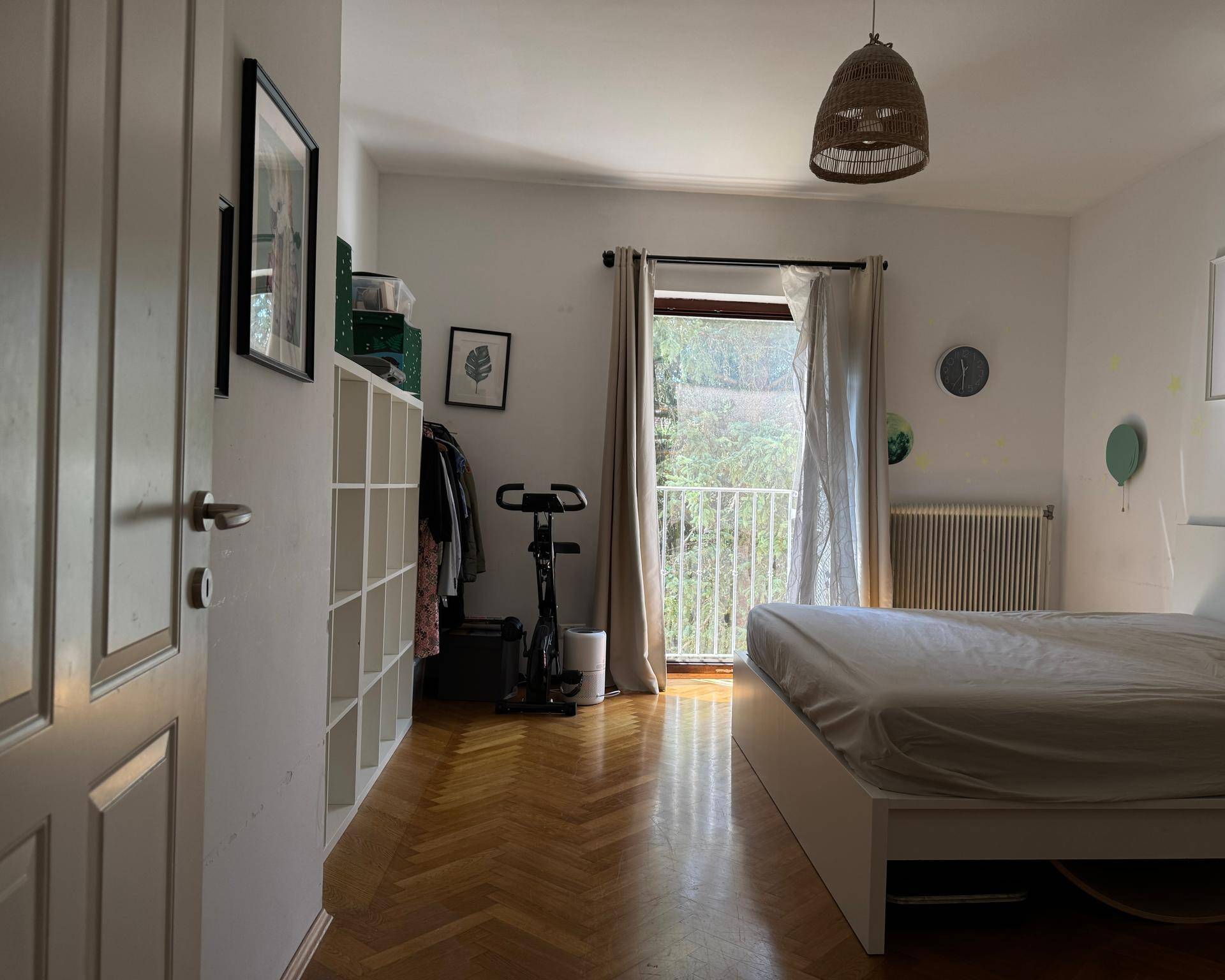 Schlafzimmer mit Parkettboden, Bett und Zugang zum Balkon, bietet Platz für Sportgeräte.