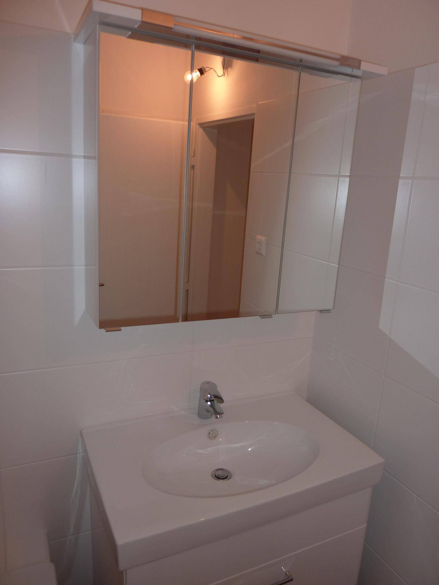 Waschbecken mit Unterschrank und Spiegelschrank in einem hell gefliesten Badezimmer.