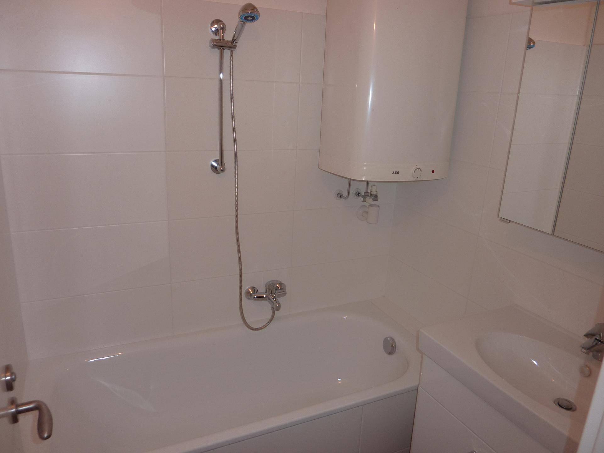 Badezimmer mit weißen Fliesen, Badewanne mit Duschfunktion und einem Waschbecken mit Unterschrank.
