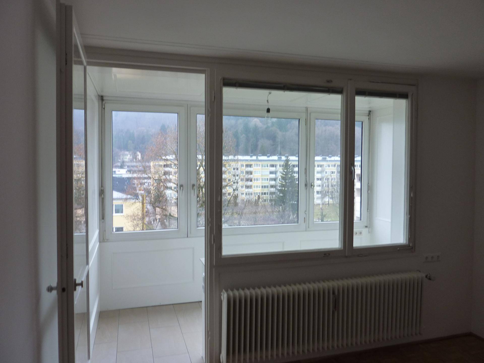 Heller Raum mit großen Fenstern und Blick auf die umliegende Stadt und bewaldete Hügel.