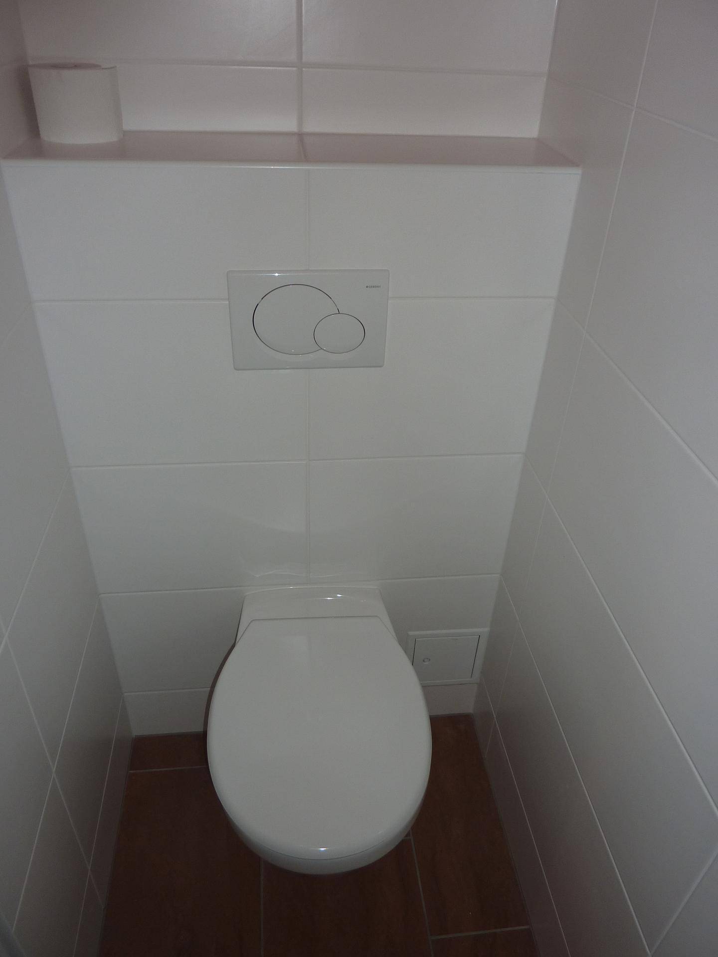 Separate Toilette mit weißen Wandfliesen und dunklem Boden, funktional und sauber.