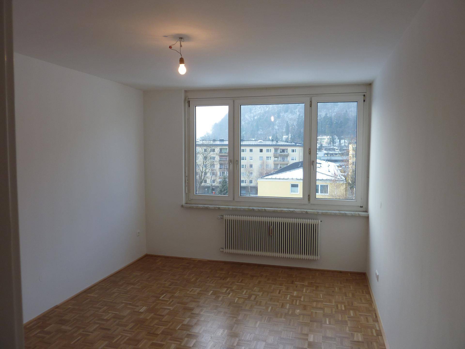 Helles Schlafzimmer mit Parkettboden und großem Fenster, das einen Blick auf die Umgebung bietet.