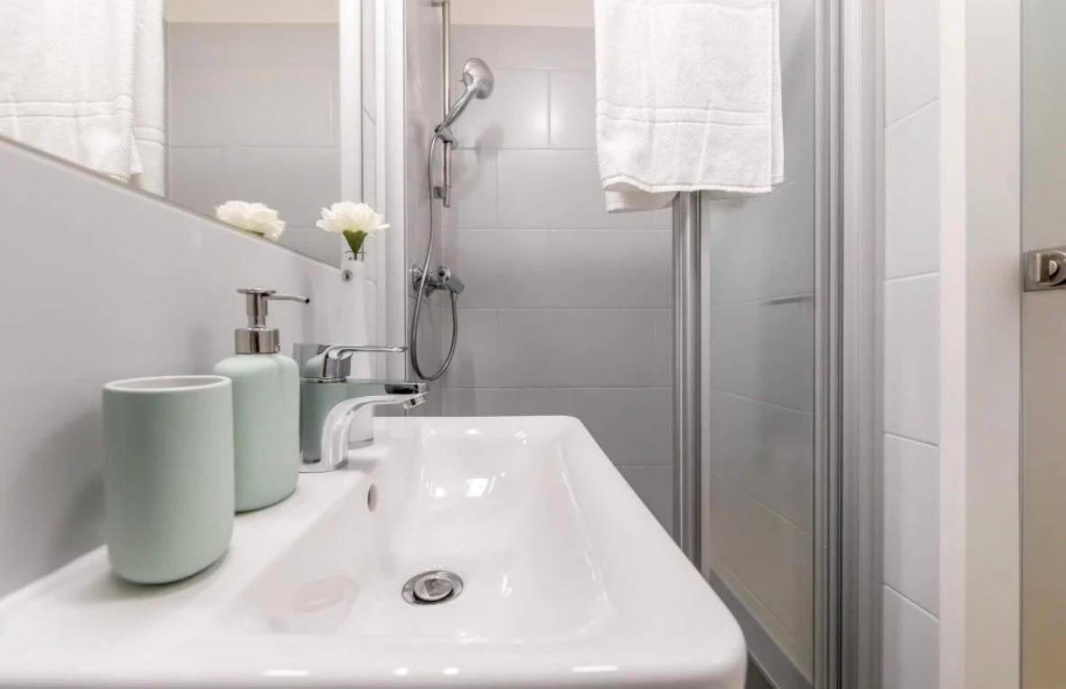 Modernes Badezimmer mit Waschbecken, Spiegel und Duschkabine in hellen Grautönen.