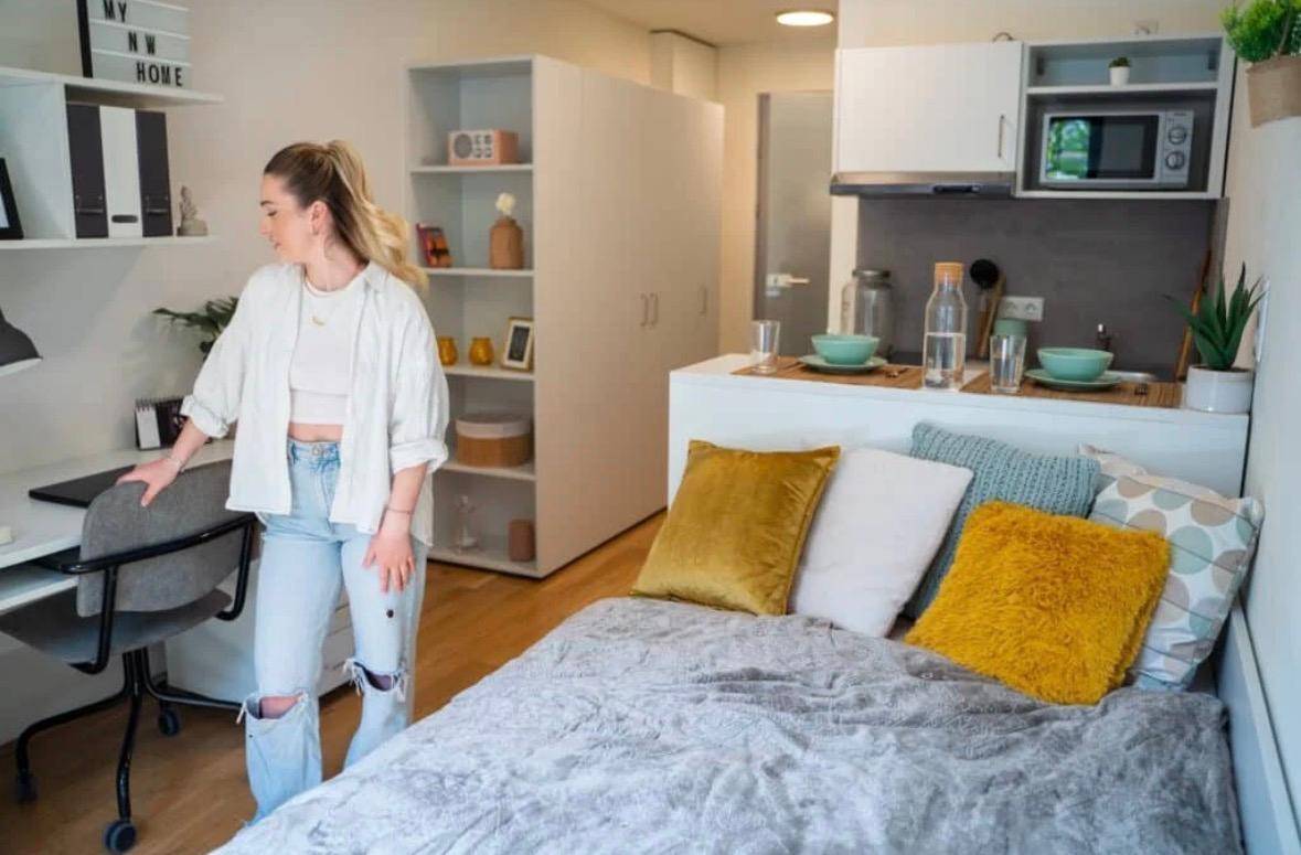 Modernes Studio-Apartment mit Schreibtisch, Regalen, Bett und kompakter Küchenzeile.