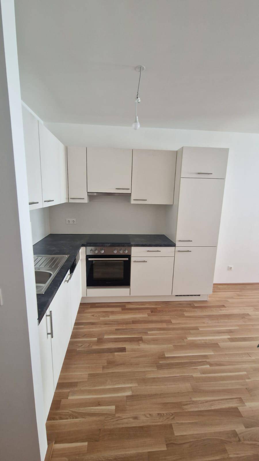 Moderne Einbauküche mit weißen Schränken, dunkler Arbeitsplatte und integriertem Backofen.