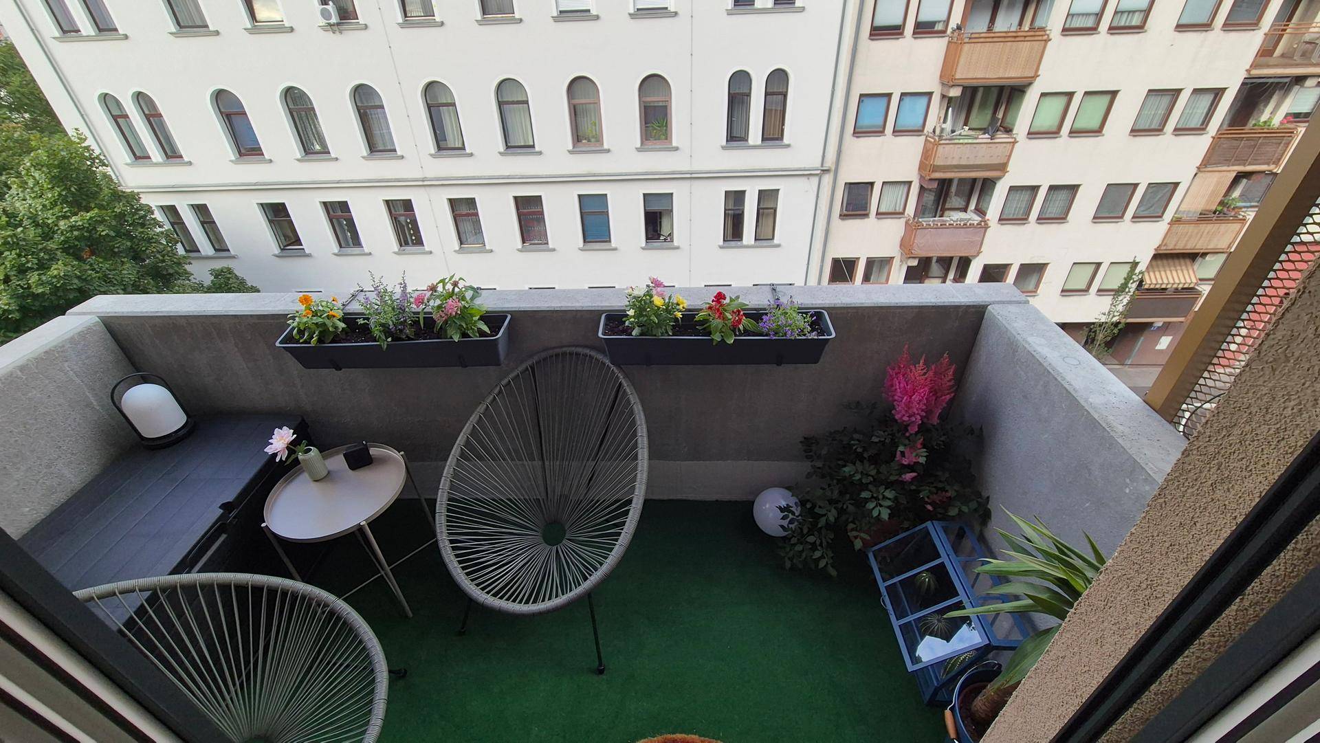 Gemütlicher Balkon mit Sitzgelegenheiten, Pflanzen und Blick auf die umliegenden Gebäude.