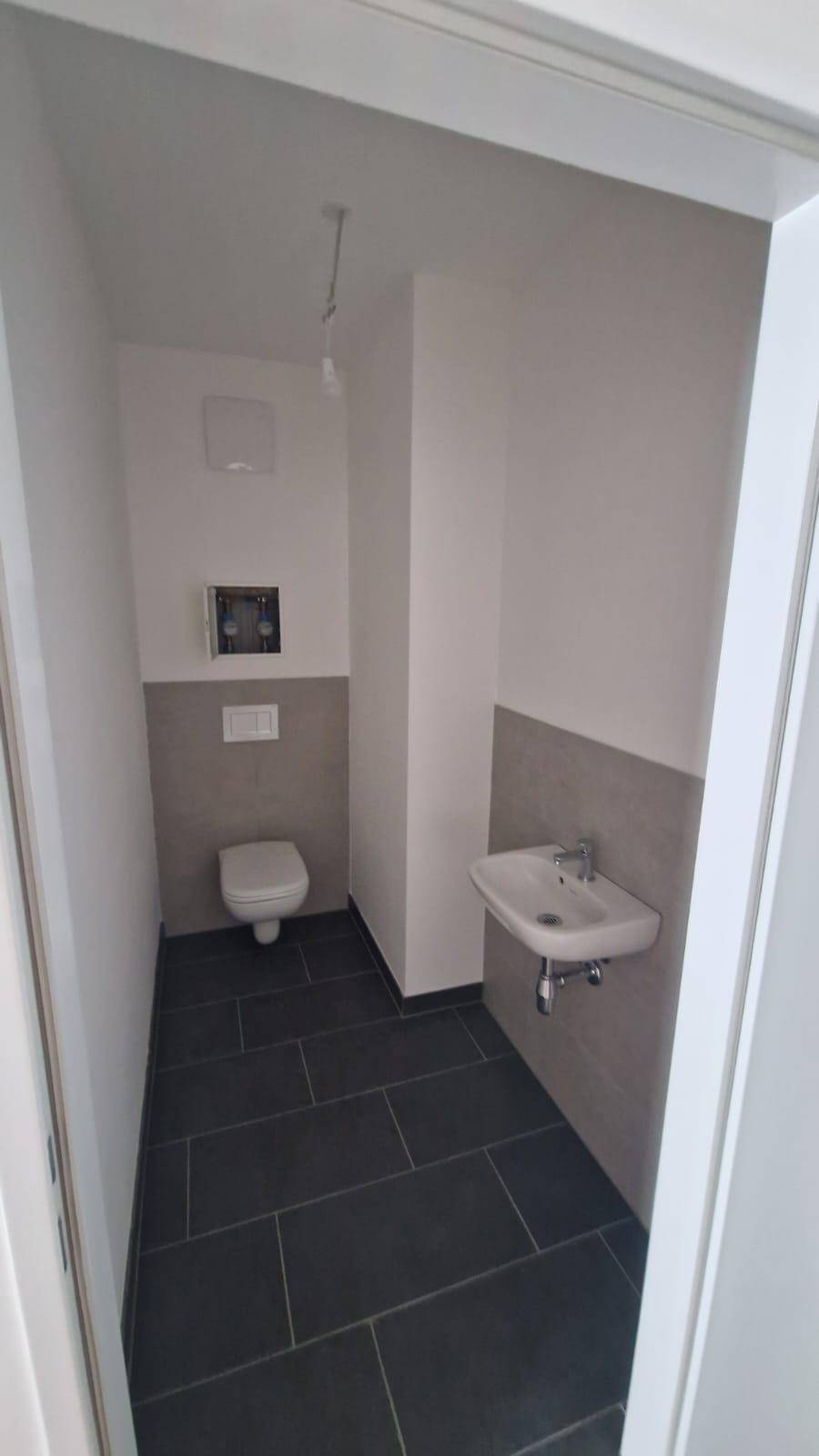 Separates Gäste-WC mit Wand-WC, kleinem Waschbecken und dunklen Bodenfliesen.