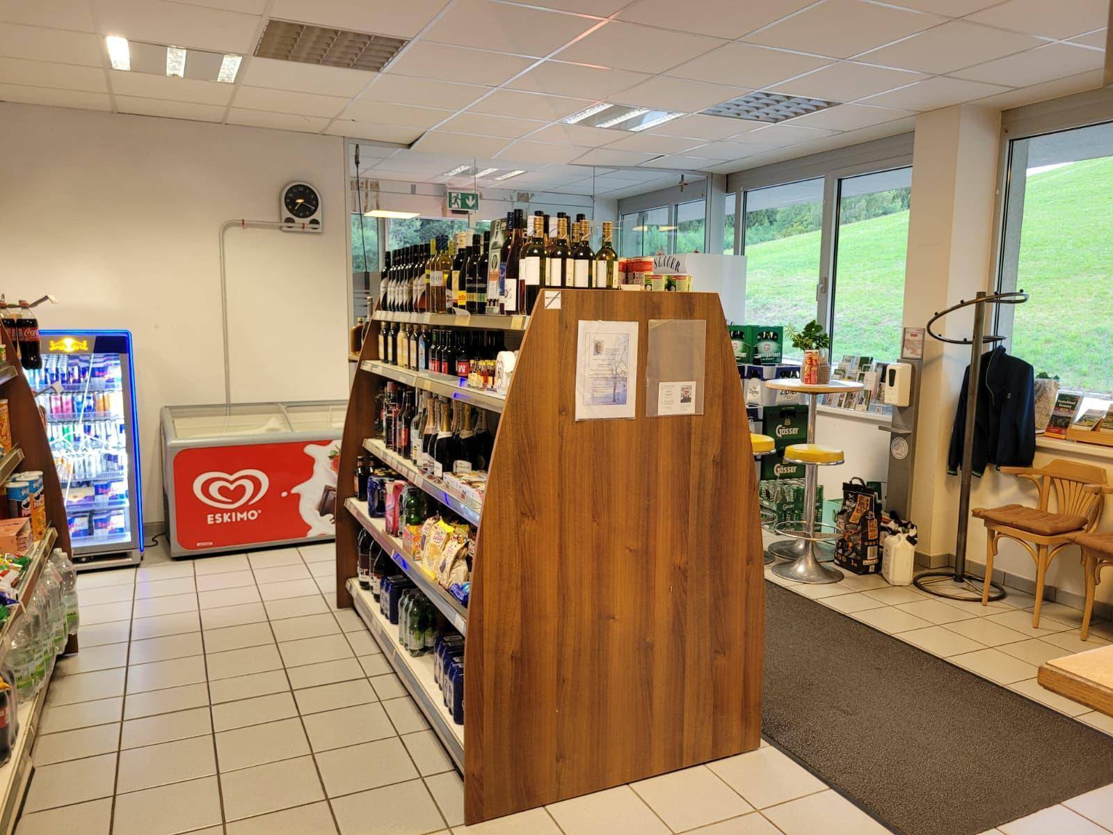 Verkaufsraum mit Regalen voller Produkte, einem Gefrierschrank und großen Fenstern zur Landschaft.