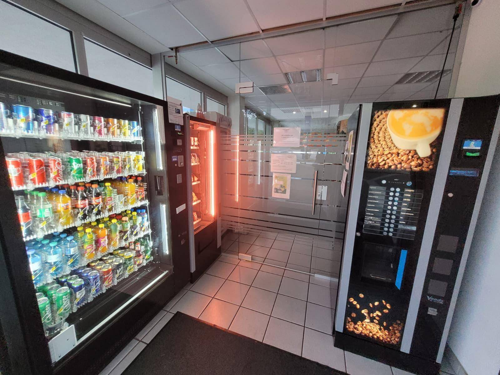 Eingangsbereich mit mehreren Verkaufsautomaten für Getränke und Snacks, hell beleuchtet.