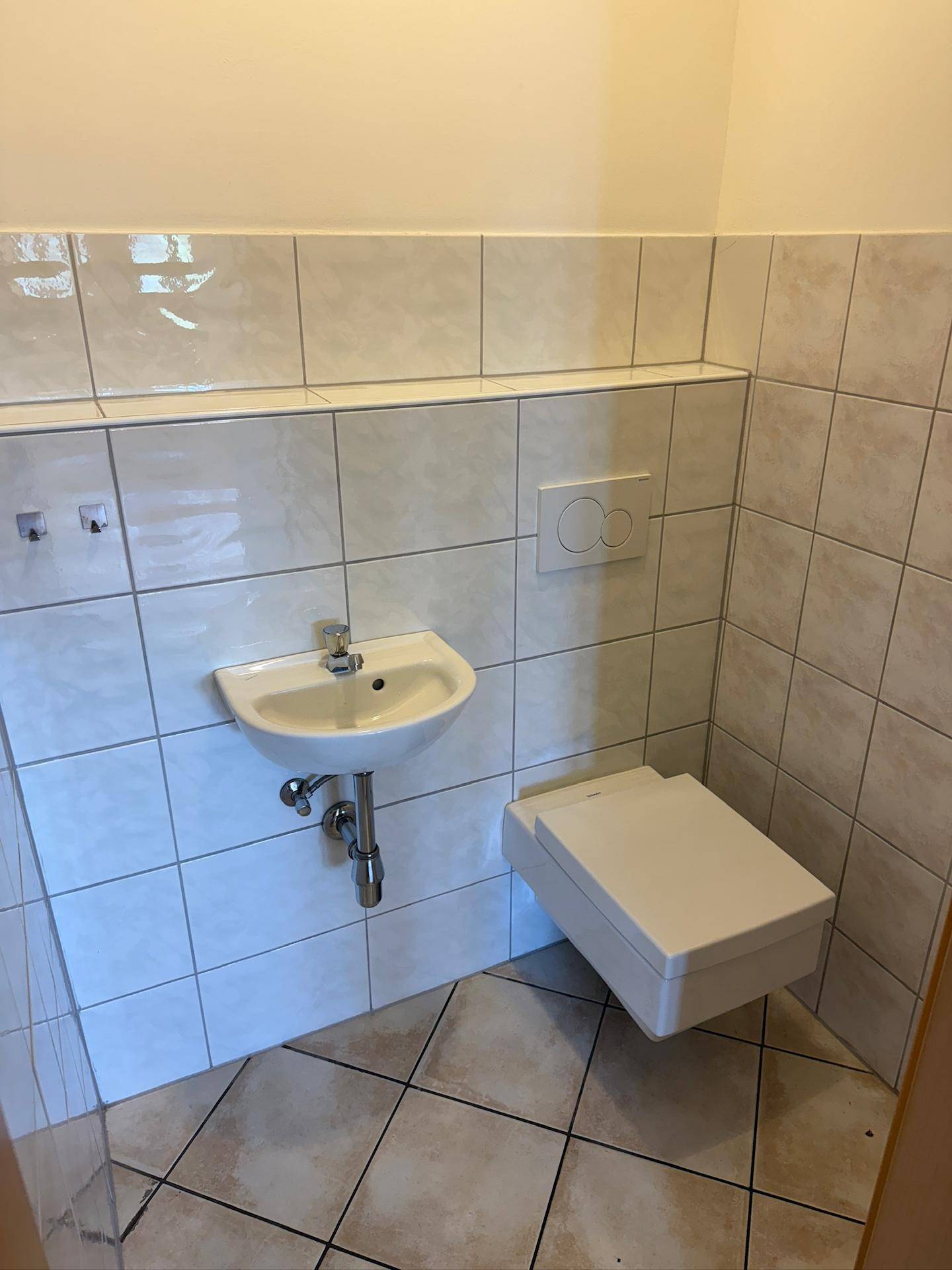 Moderne Toilette mit Wand-WC, kleinem Waschbecken und weißen Fliesen an Wänden und Boden.